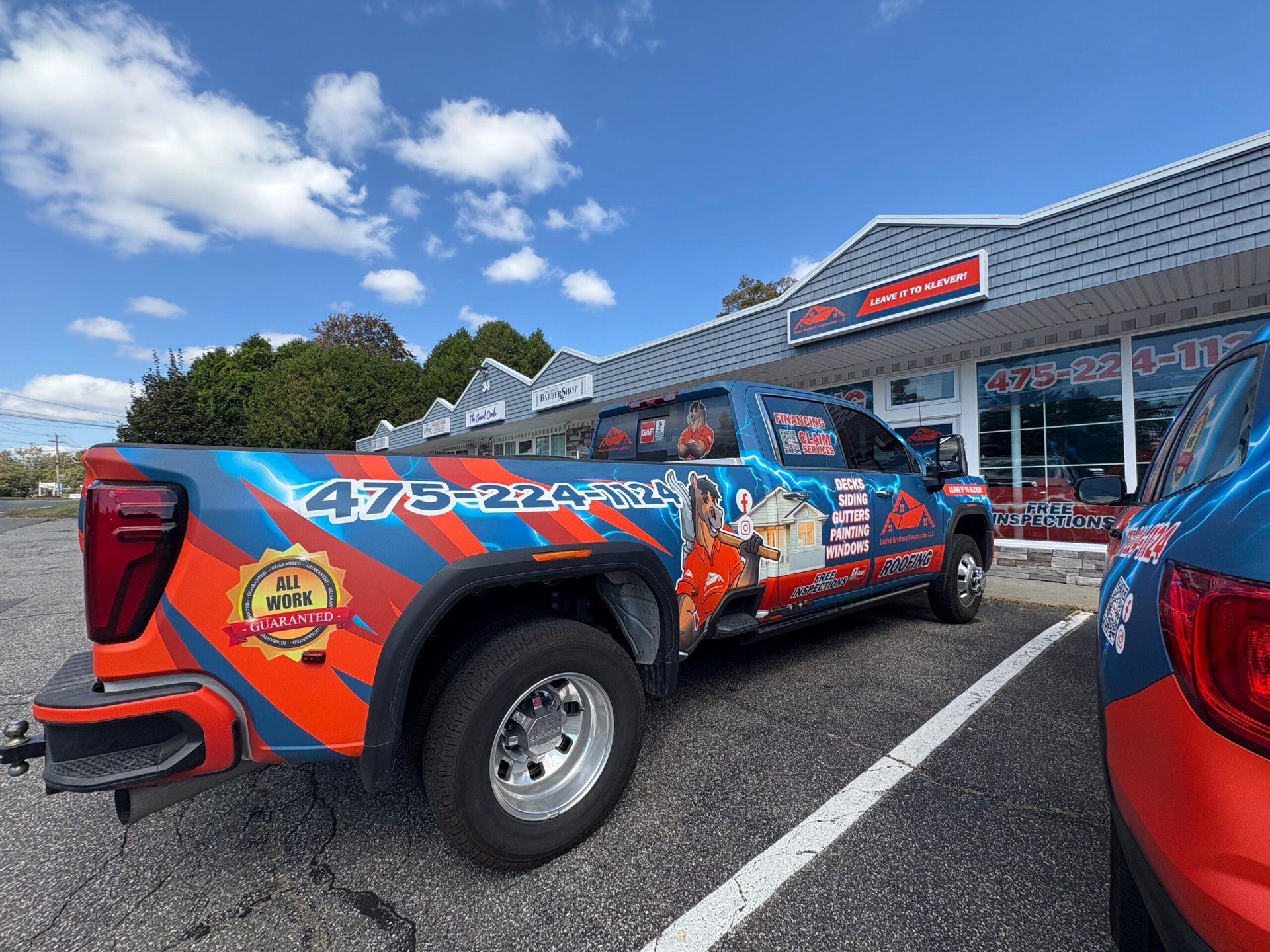 Blue-and-orange wrapped pickup truck parked outside a storefront on a sunny day