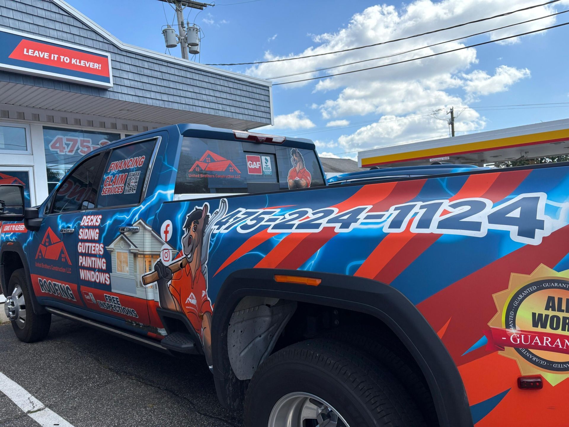 Colorful race truck with red, blue, and black graphics parked outside a storefront under a sunny sky