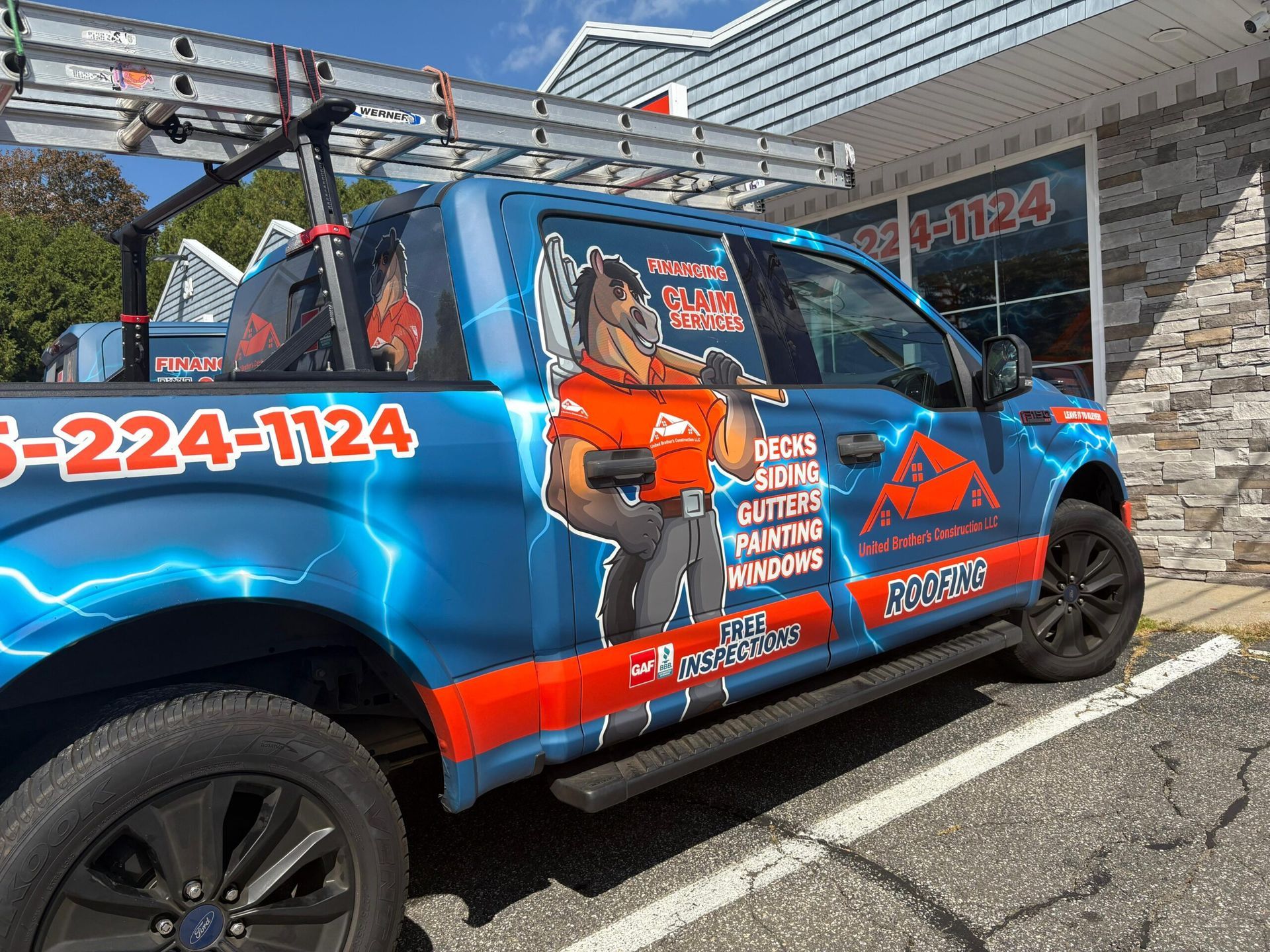 Blue-orange moving truck parked outside a building with a large ladder on top and company graphics on the side