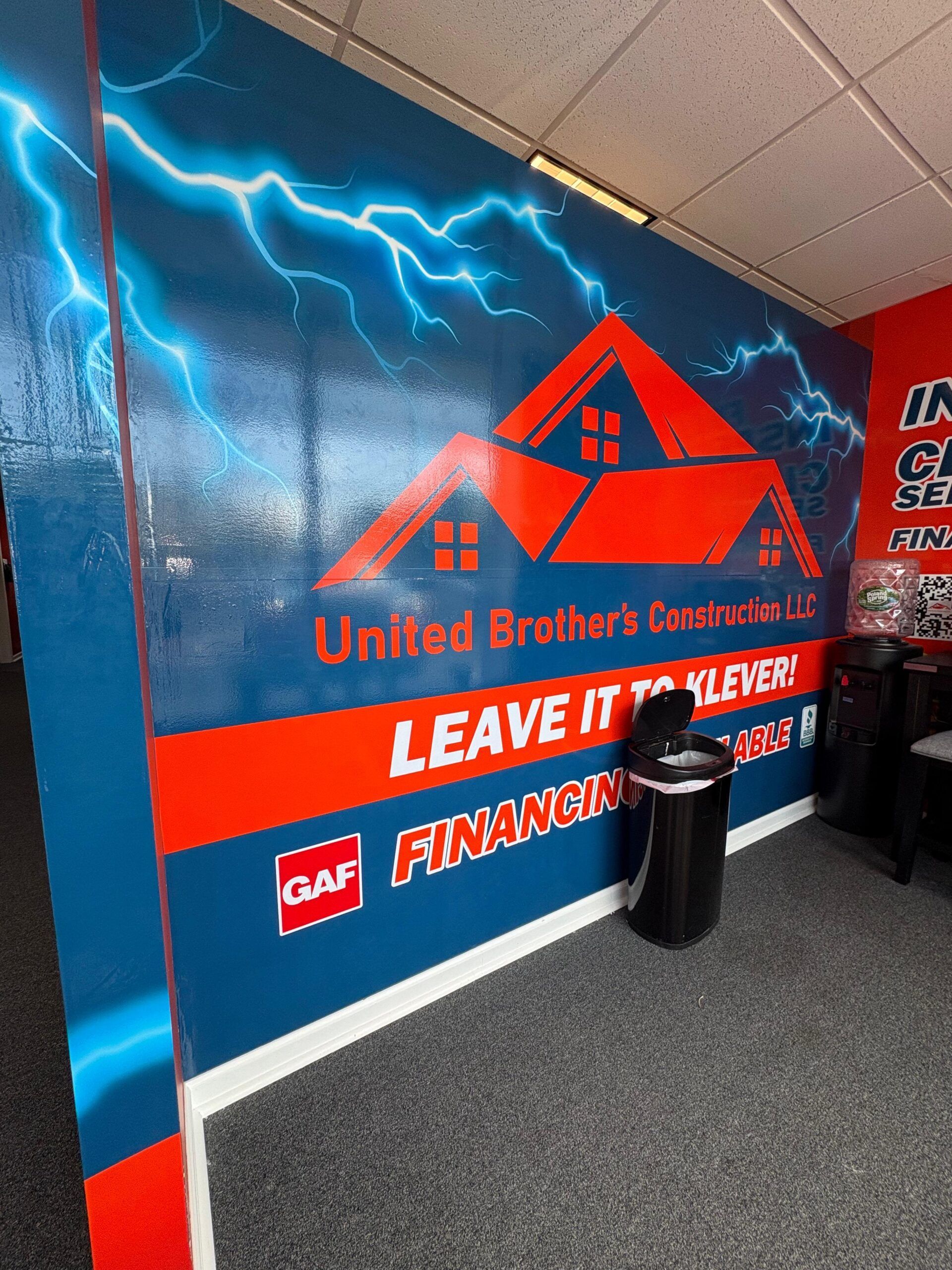 Branded wall mural with lightning, United Brothers Roofing logo, red “Leave it to…” sign, and trash can