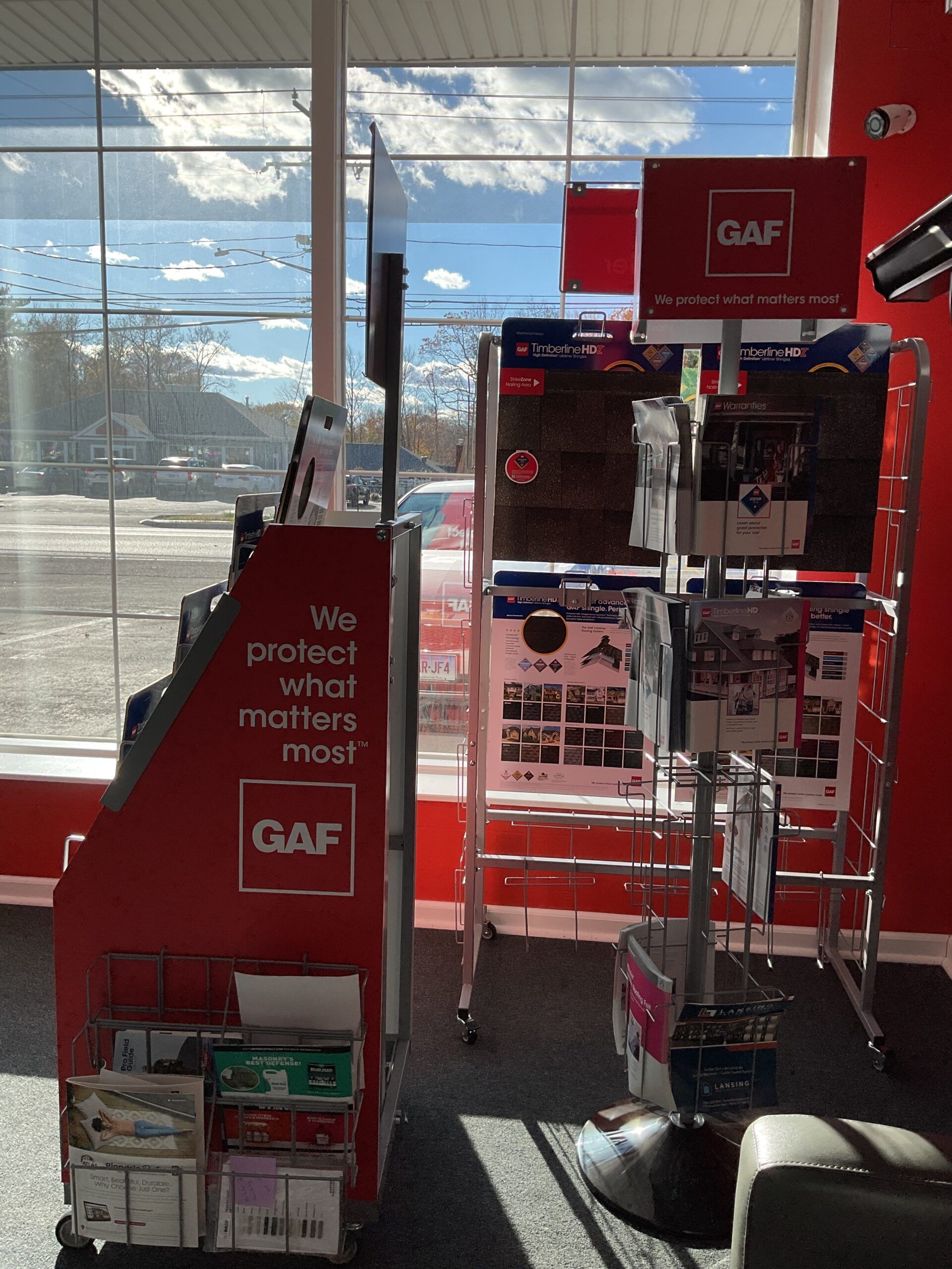 Red GAF store display with brochures and a sign by a bright window inside a retail shop