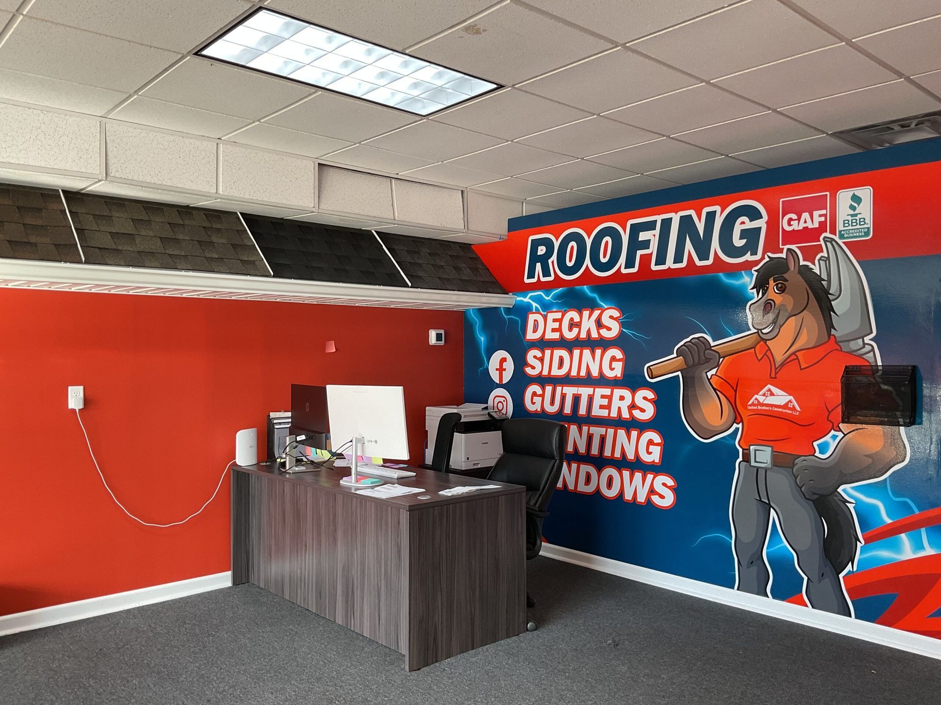 Roofing office reception with red walls, desk, and large mural advertising decks, siding, gutters, and windows