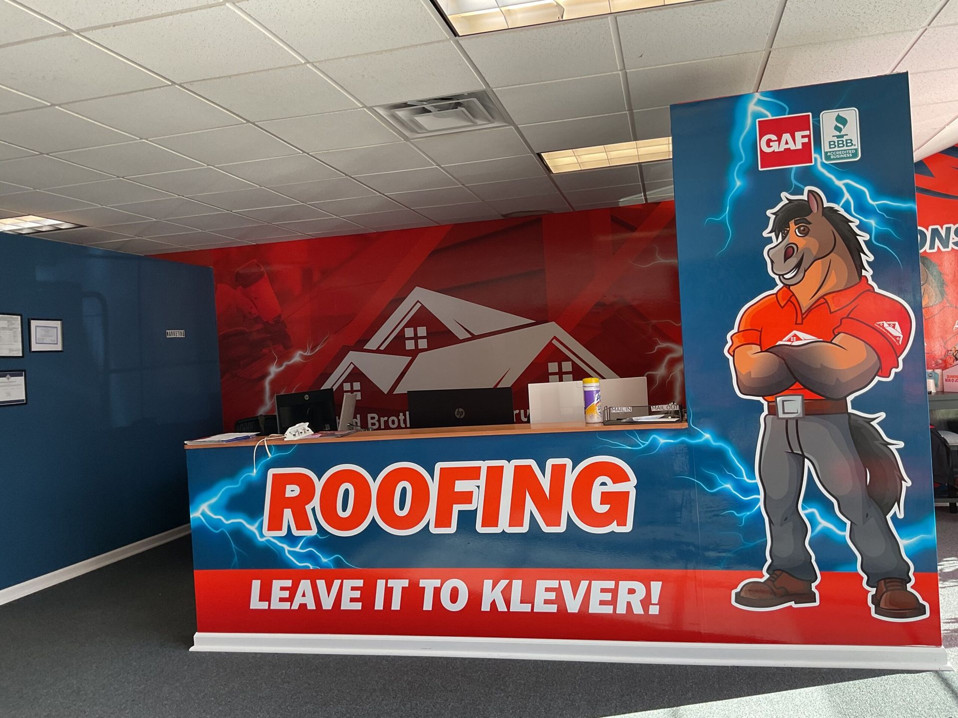 Roofing company booth with red banner reading “LEAVE IT TO KLEVER!” and a cardboard worker cutout