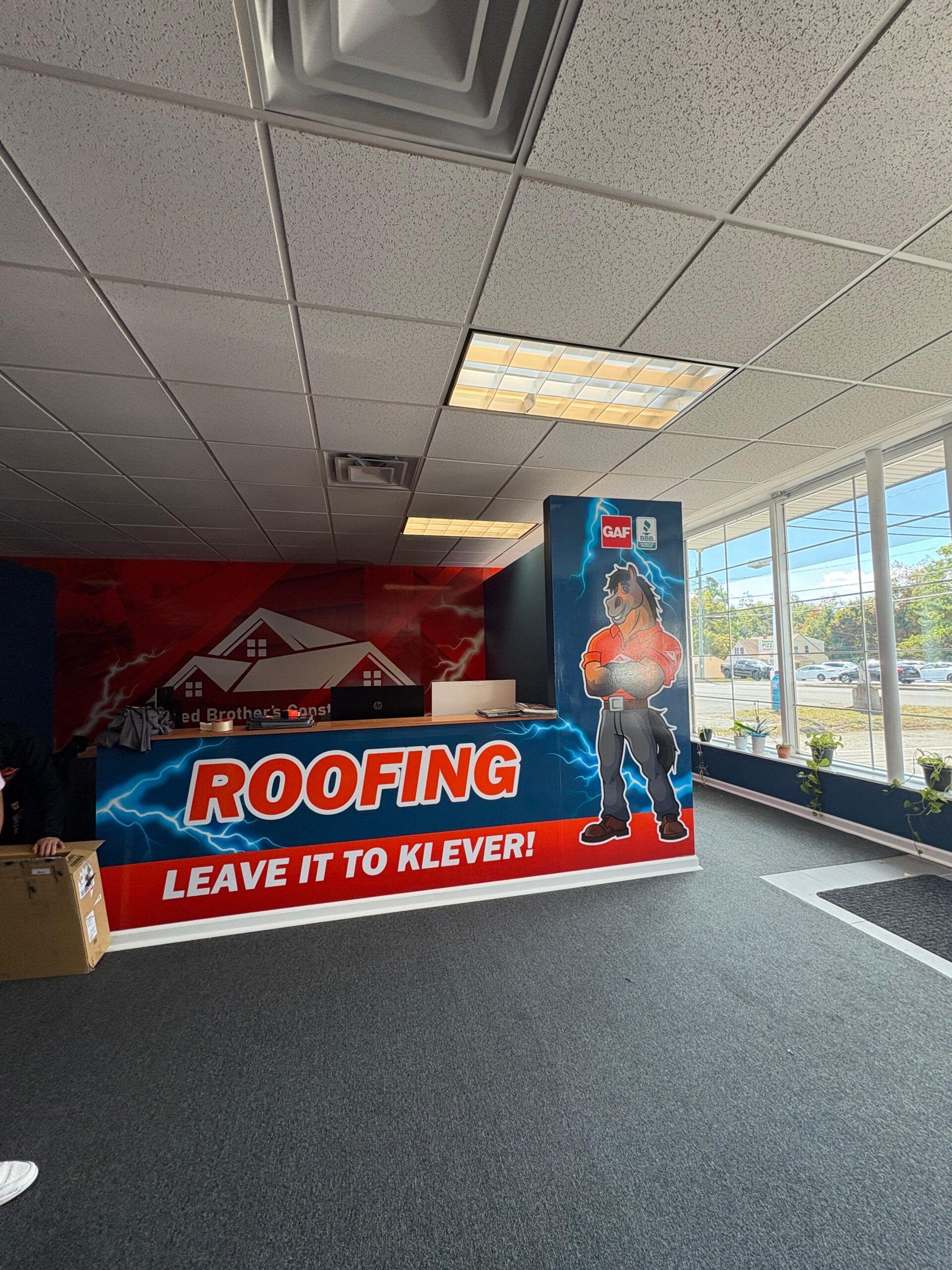Red roofing company banner in an office lobby with a cardboard cutout display and large windows