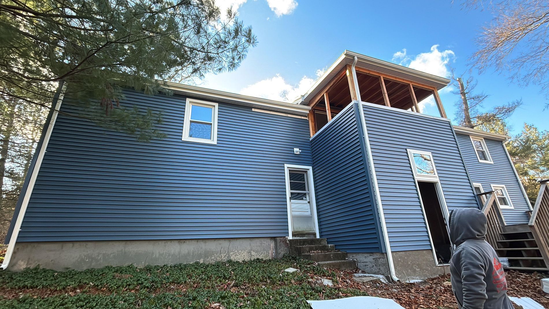 Blue house under construction with a worker on a roofed porch and a ladder in front