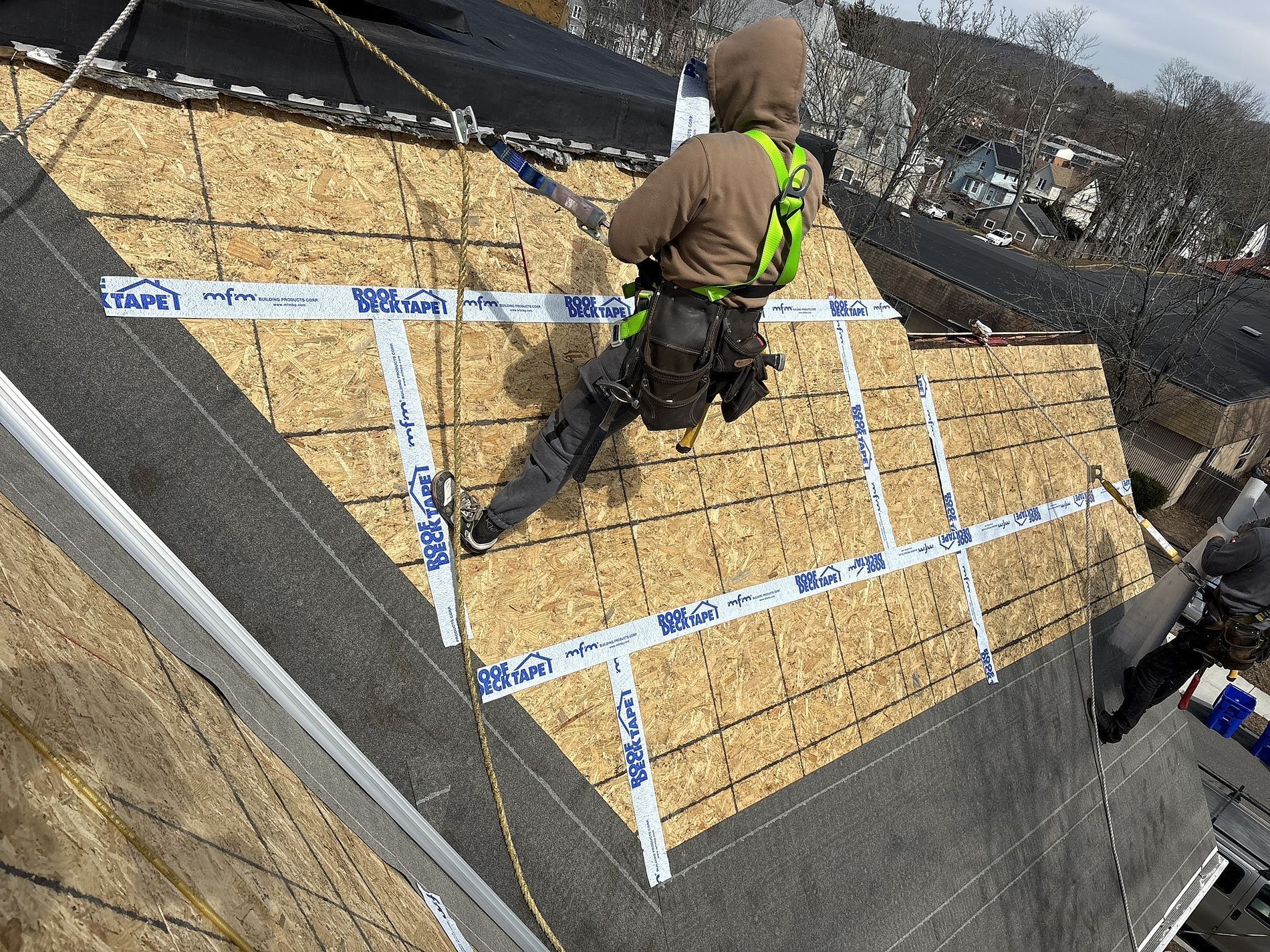 Worker installing roof insulation panels on a sloped roof, with blue tape grid markings and safety harness.