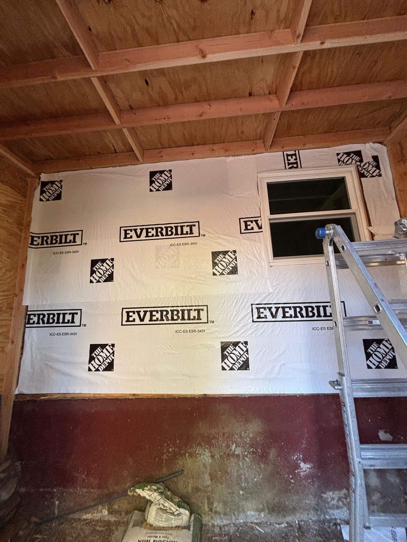 Partially finished room with insulated wall, open window, and a ladder leaning inside.