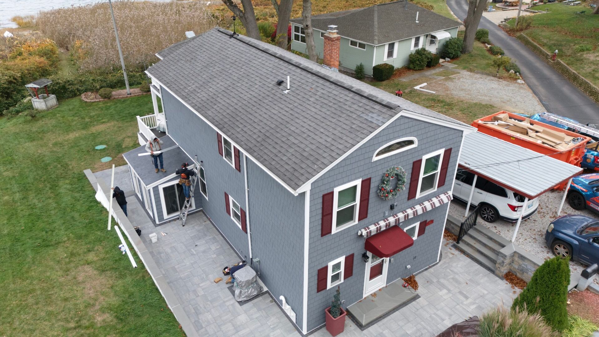 Aerial view of a gray two-story house with red shutters and a small patio beside a parked truck.