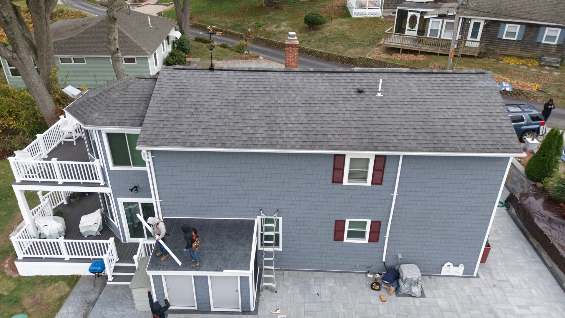 Aerial view of a gray house with white trim, small deck, and two people on the back patio.