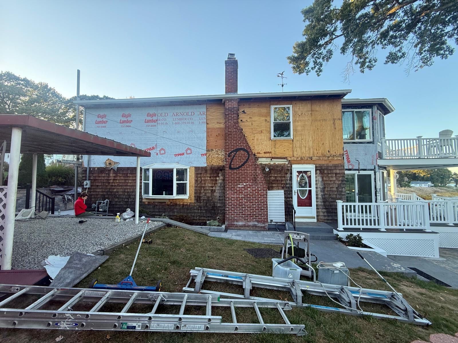 Damaged house with exposed brick, missing siding, broken windows, and debris in the yard after storm damage