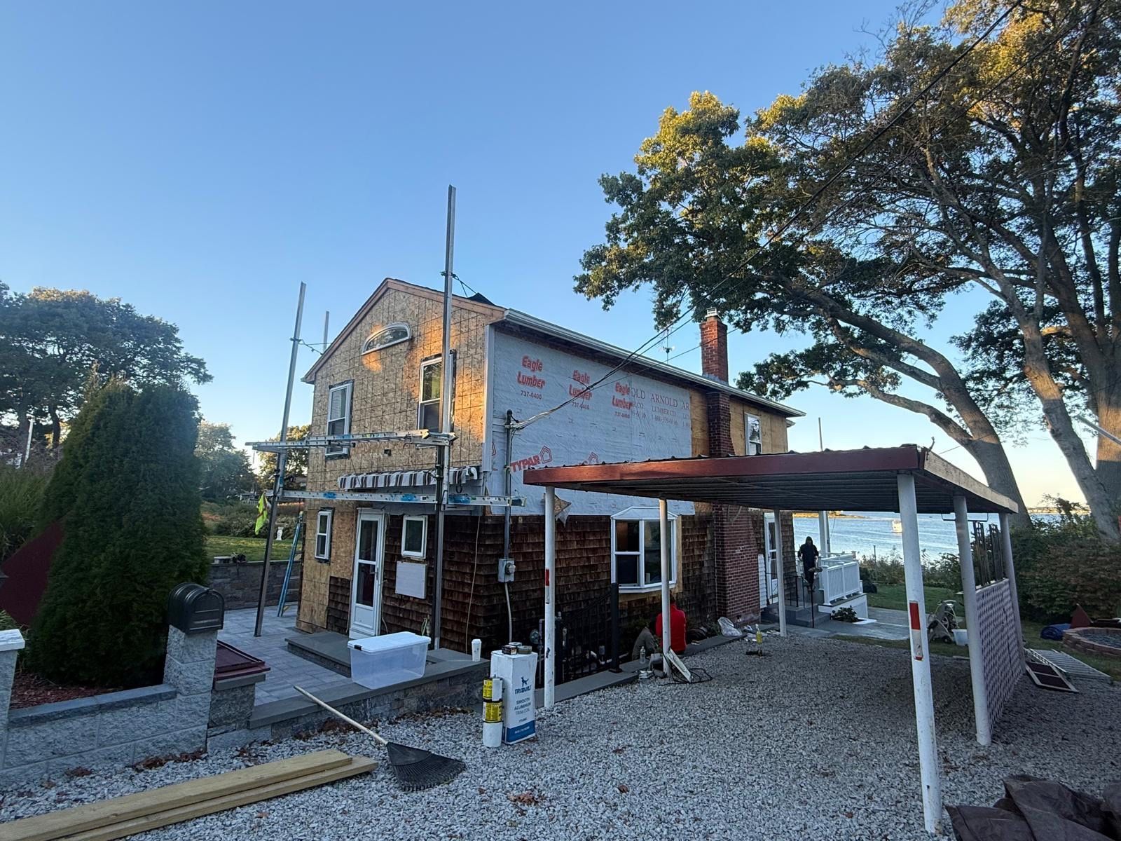 Gravel courtyard with a small two-story building, white trim, red canopy, and trees at sunset.