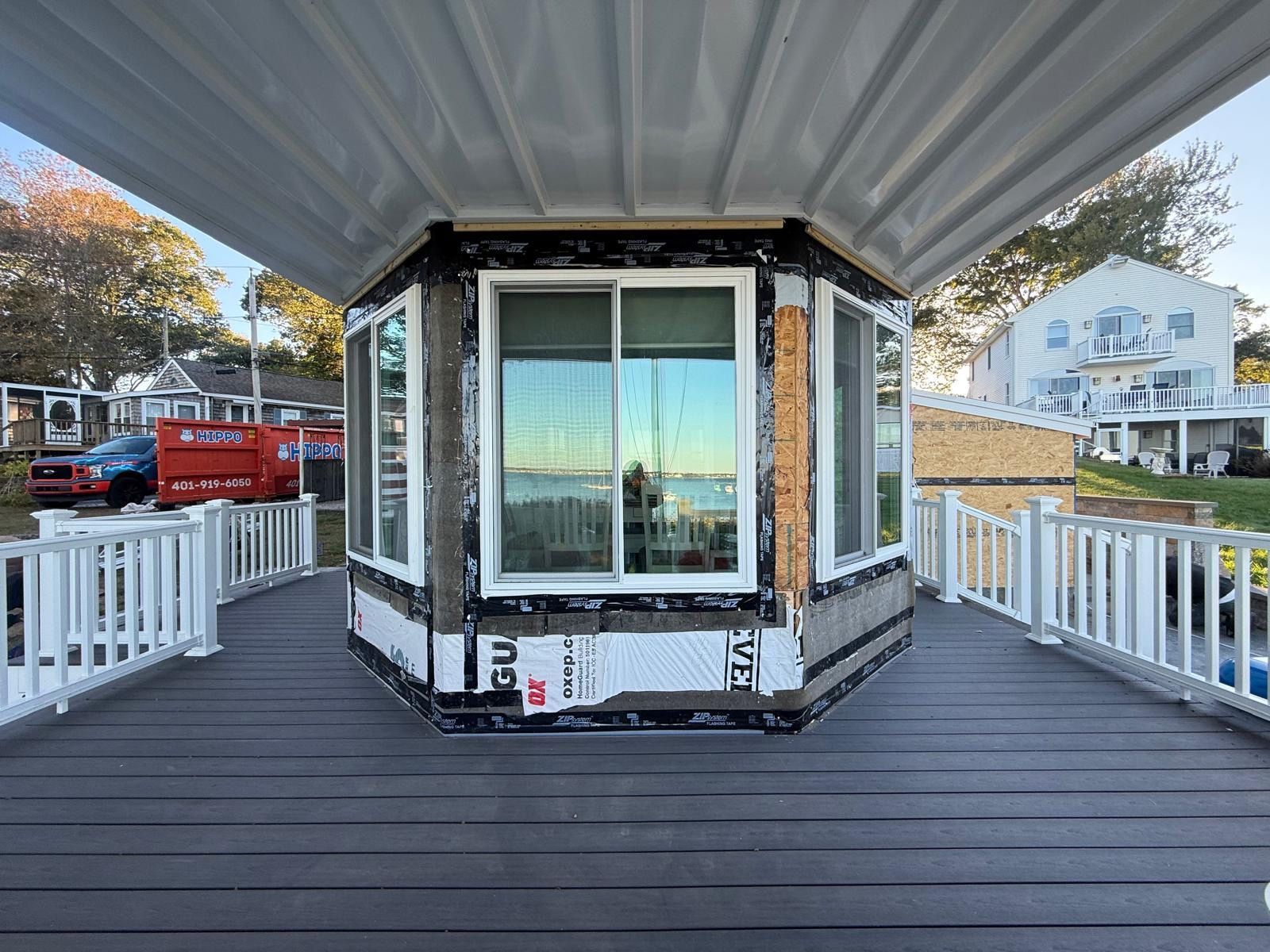 Front view of a small octagonal glass kiosk on a covered deck with white railings and water nearby
