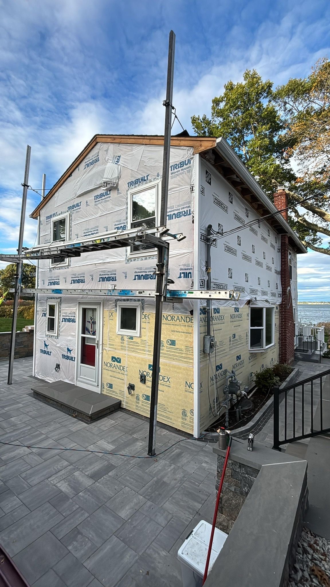 Partially renovated two-story house with scaffolding, under blue sky, on a paved street corner