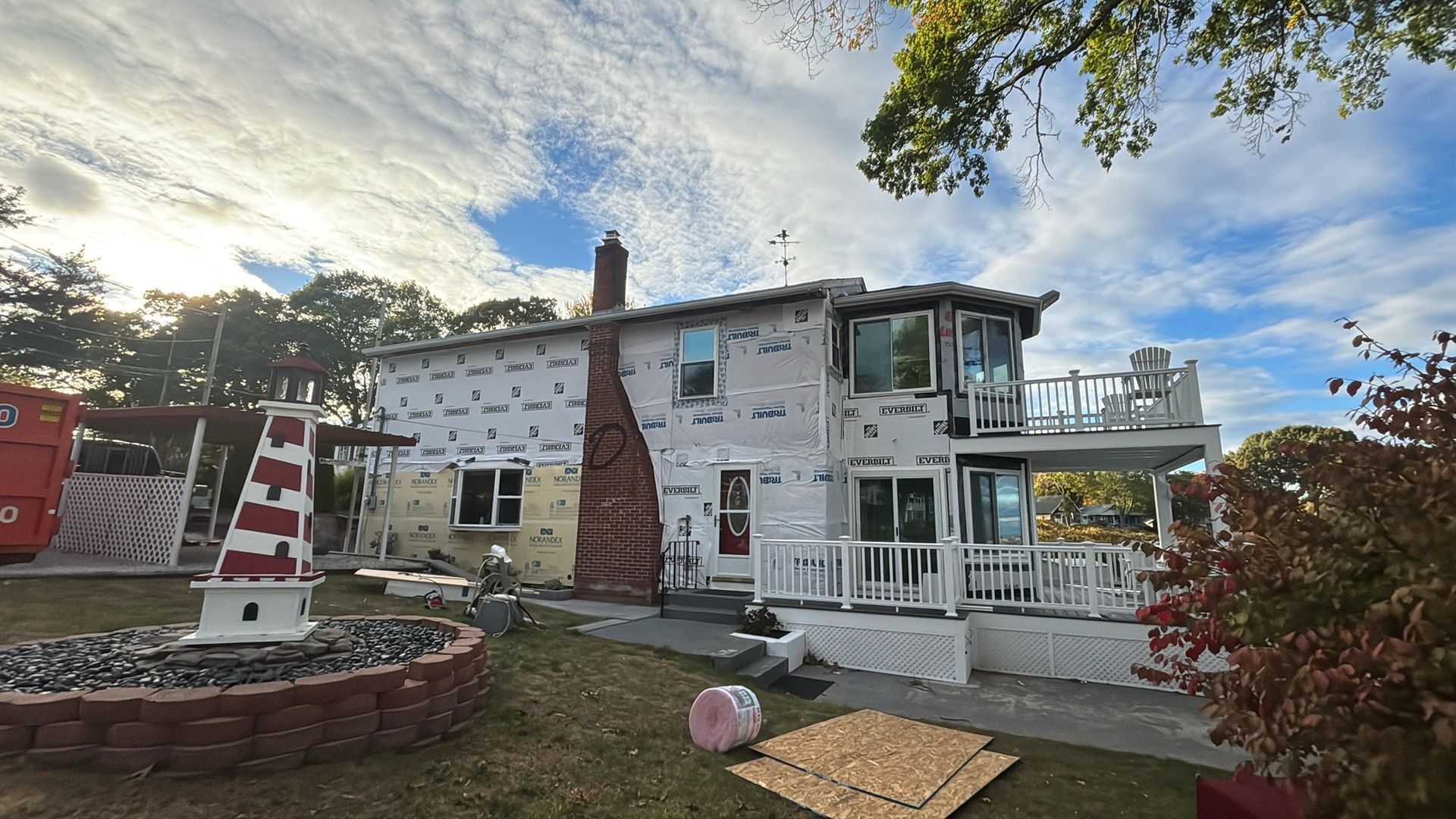 White house with porch and red-striped lighthouse lawn ornament in a yard under a cloudy sky.