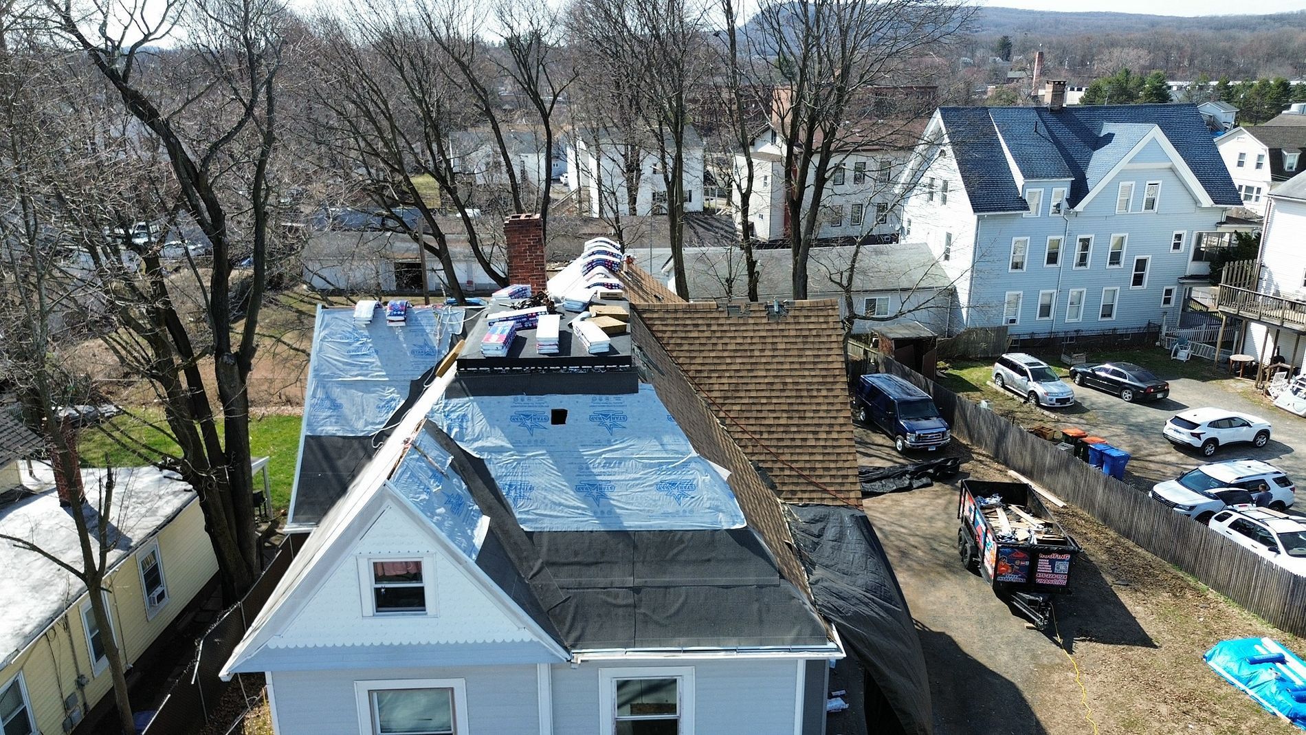 Aerial view of rooftops, a white house, and a tree-lined residential yard in early spring.