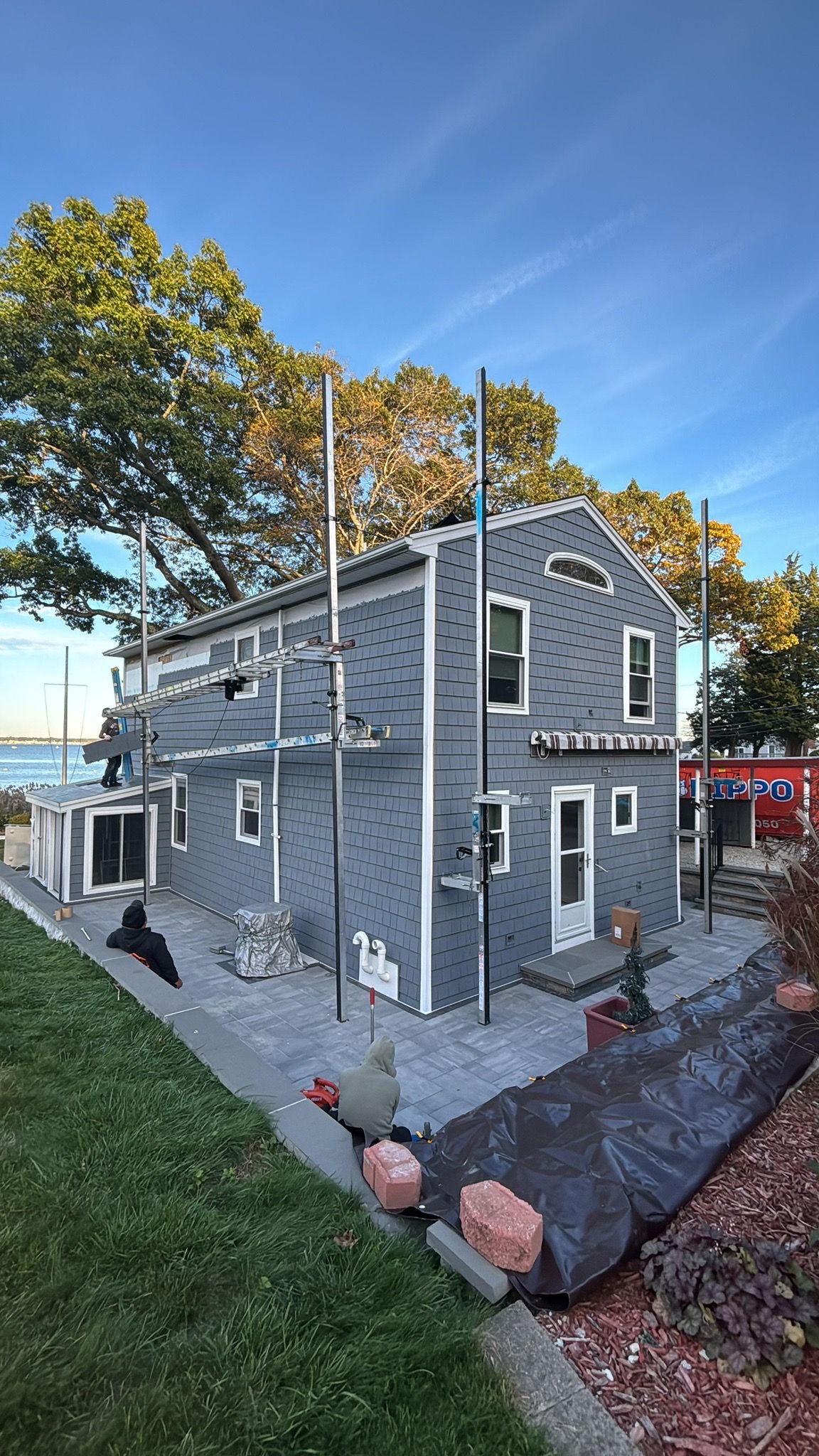 Gray house with white trim and tall poles on a landscaped slope under a clear blue sky