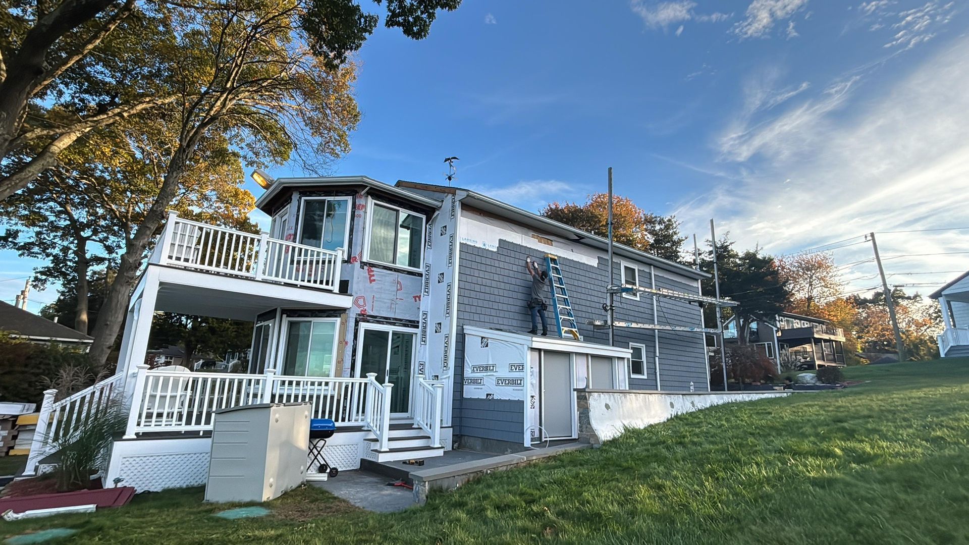Two-story gray house with white trim, porch, and steps on a grassy yard at sunset