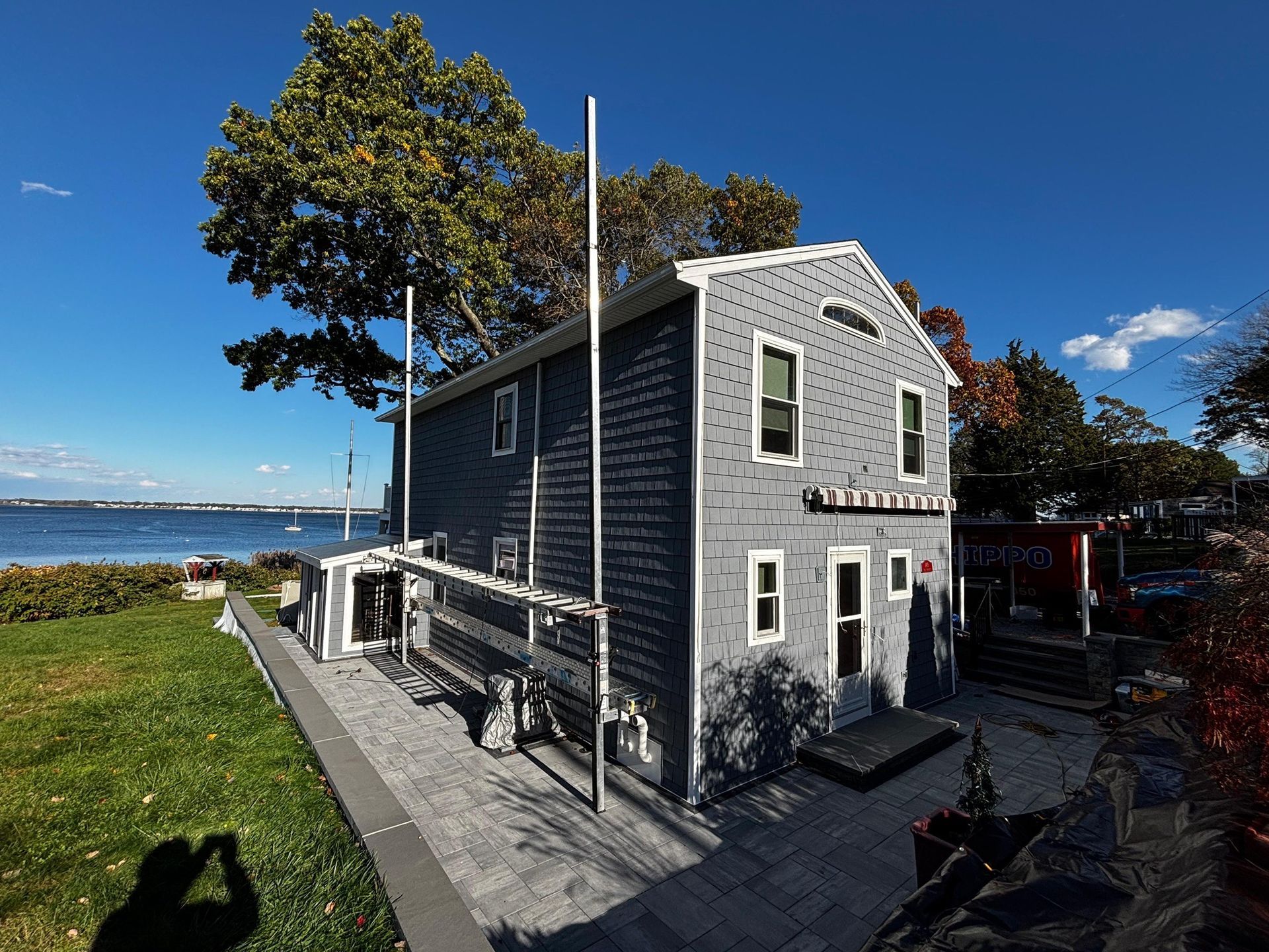 Gray seaside house with white trim beside a waterfront path under a blue sky