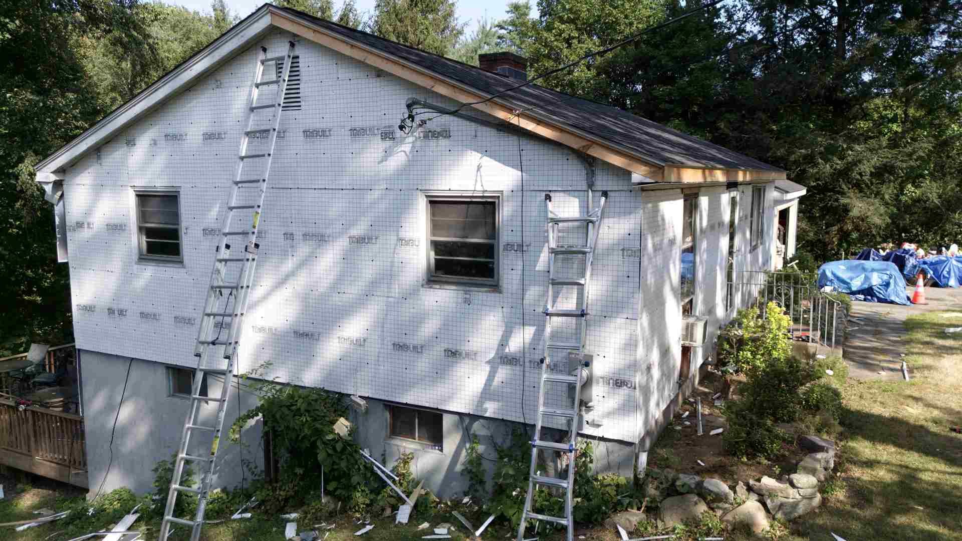 White house under renovation with ladders leaning against the exterior and construction materials nearby