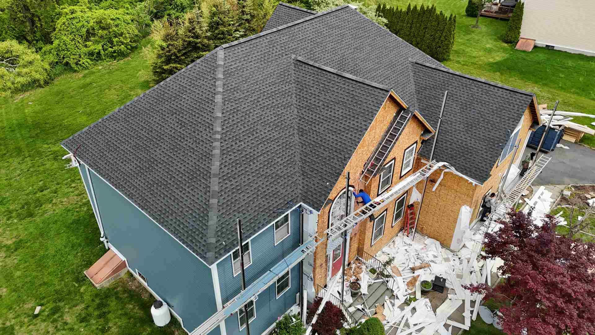 Aerial view of a house with major storm damage and debris beside the roof and exterior walls.