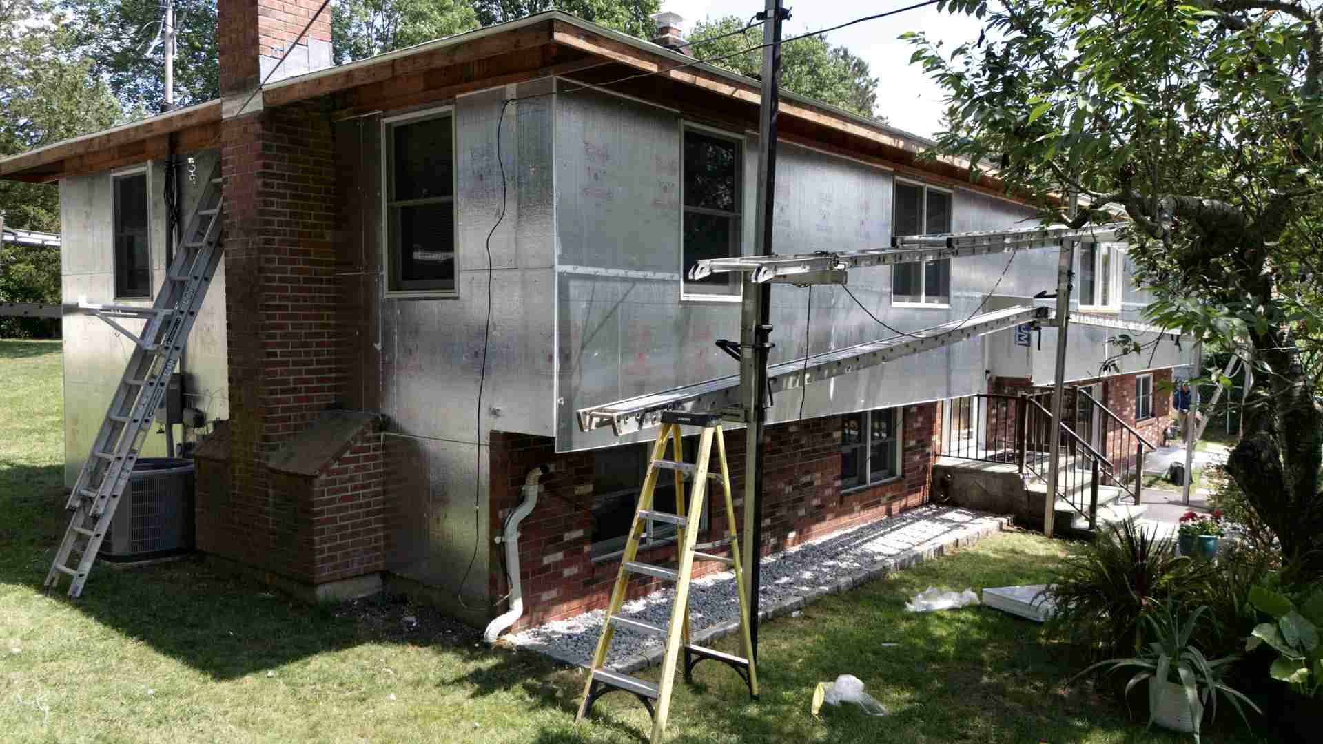 House exterior with scaffolding and ladders during renovation, white siding and brick walls visible
