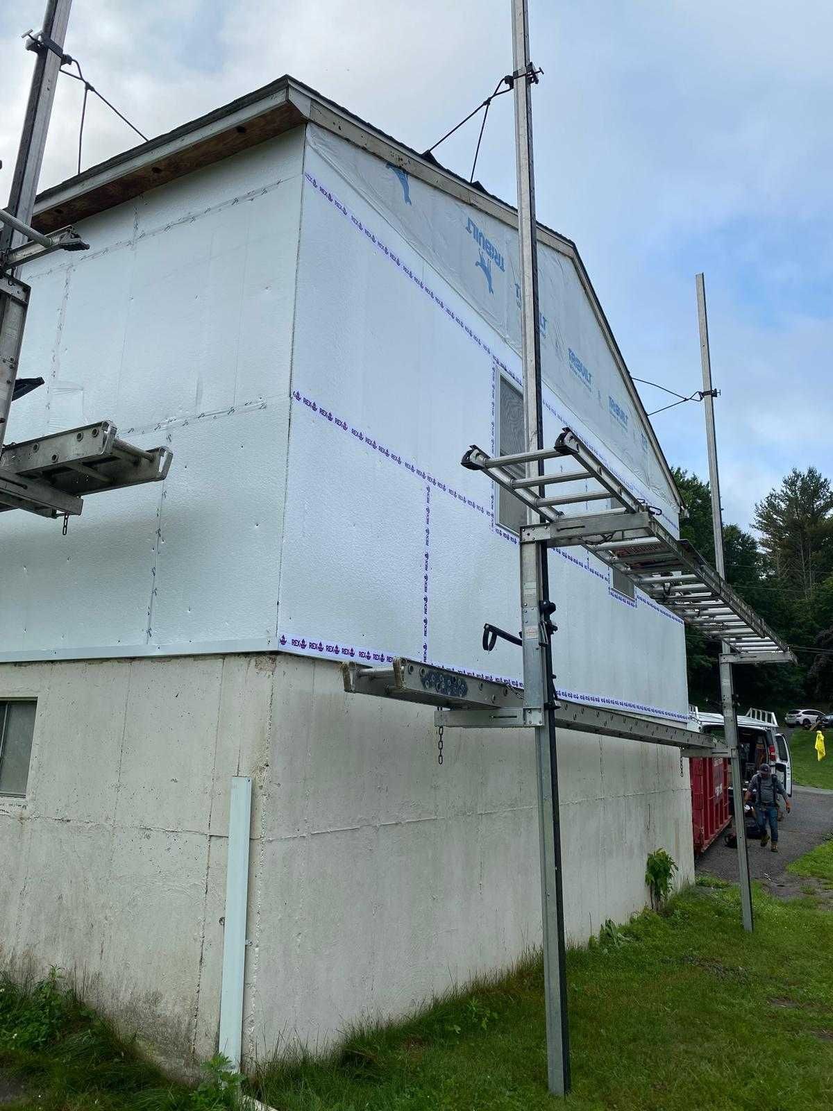Partially wrapped house with scaffolding along the side and a concrete foundation below
