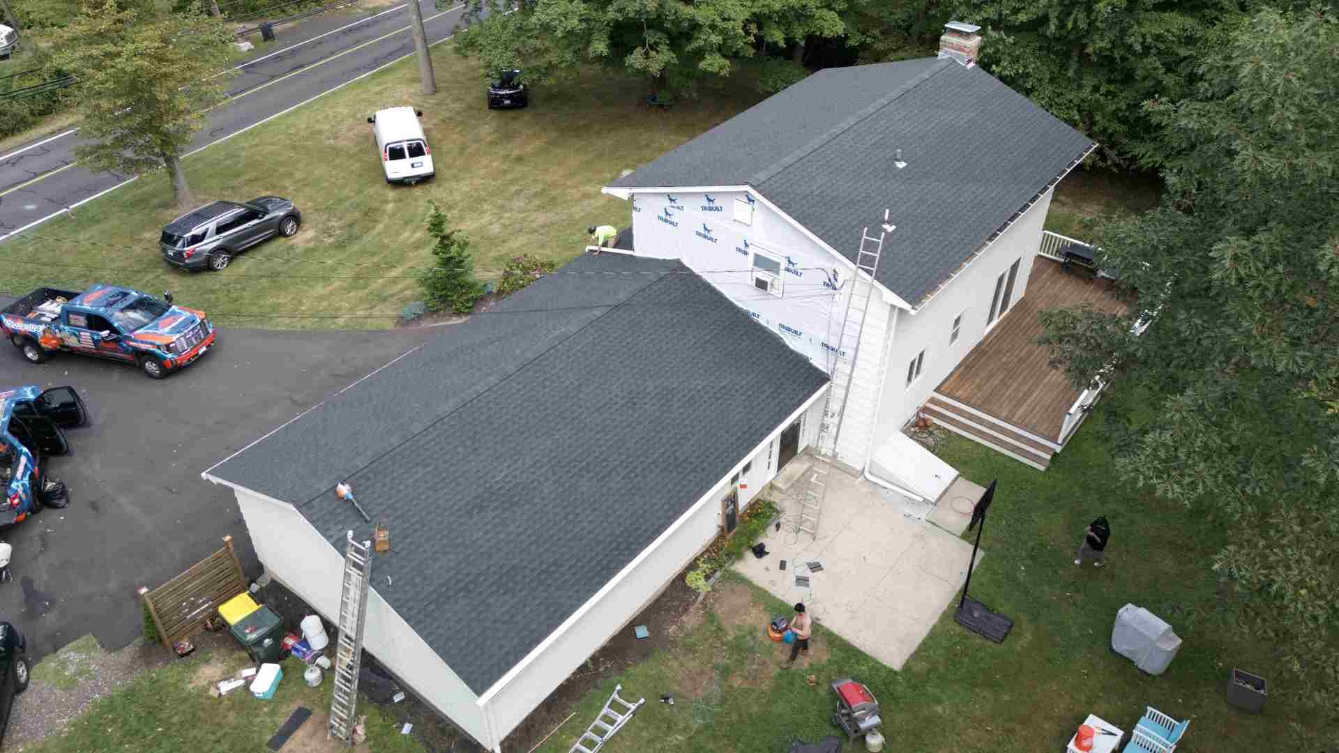 Aerial view of a house with a dark roof, driveway, parked cars, and scattered items on the lawn