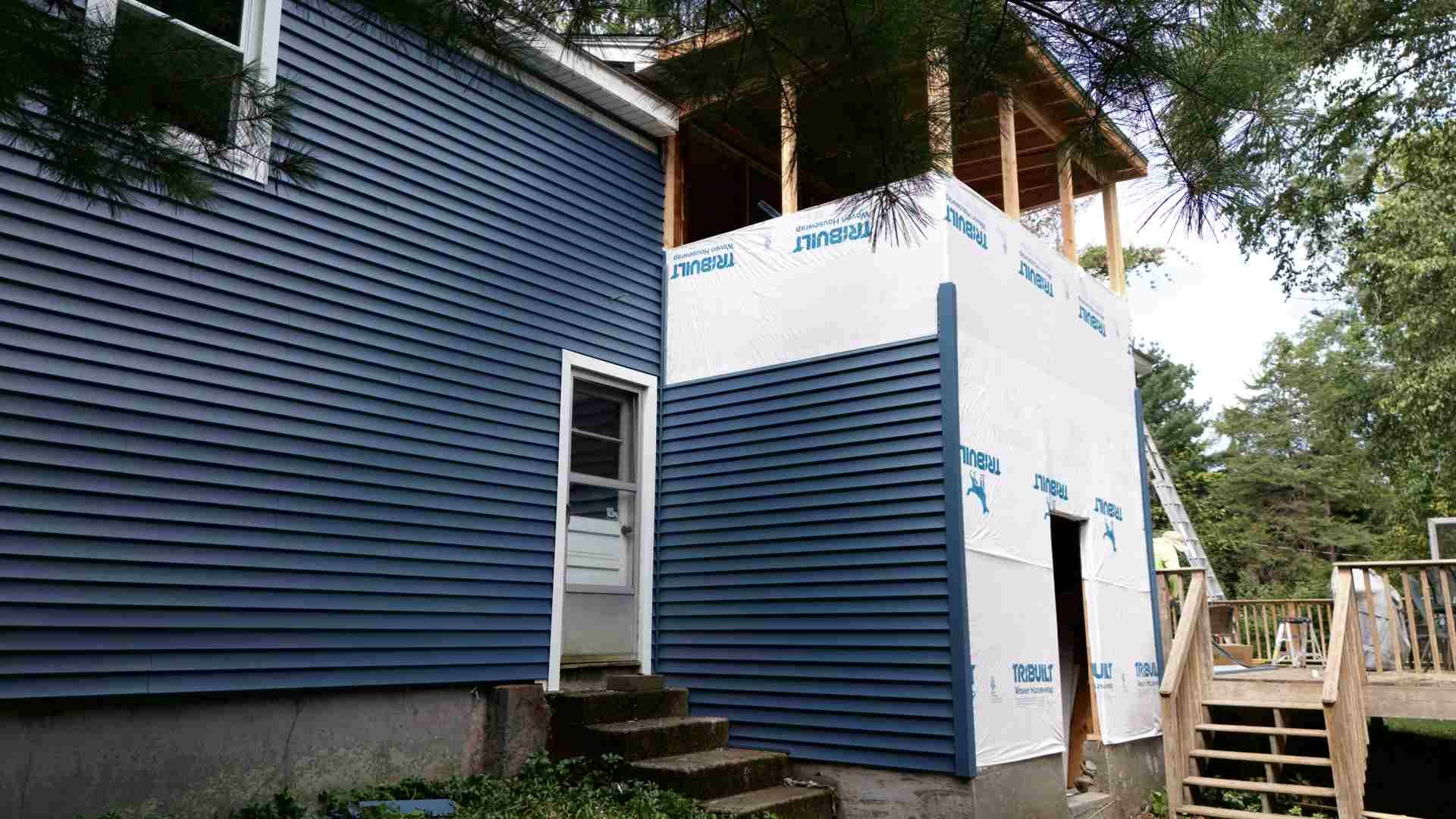 Blue-and-white house exterior with a wooden deck and stairs under trees