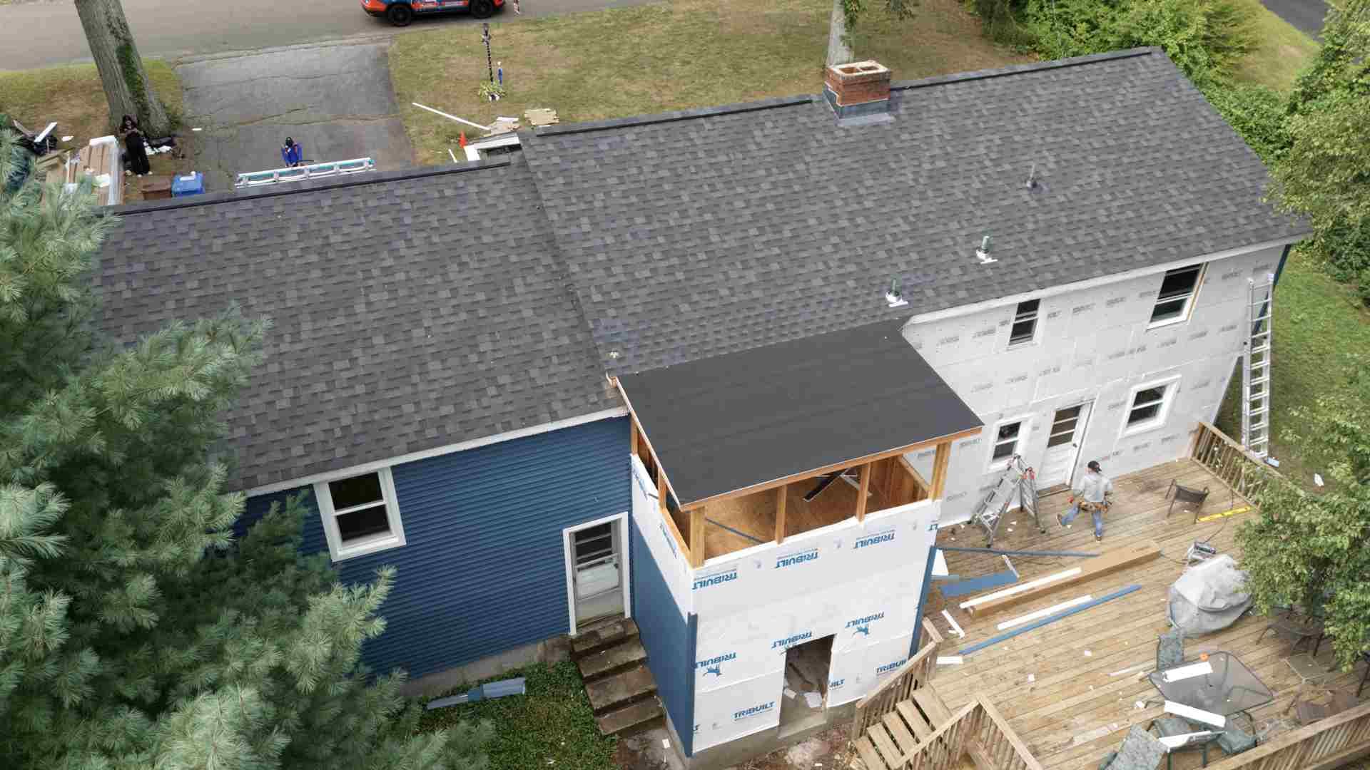 Aerial view of a house under renovation with blue siding, white addition, and exposed construction materials.