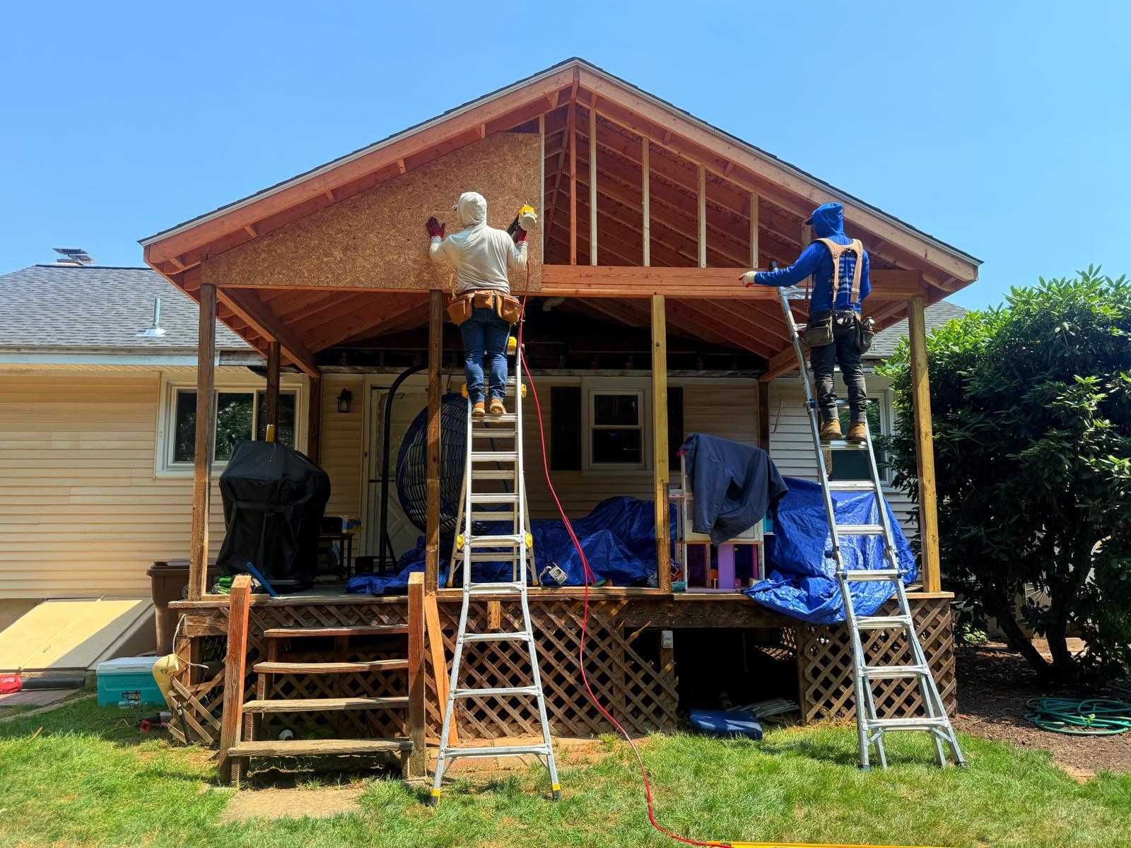 Two workers on ladders building a wooden porch roof on the front of a house