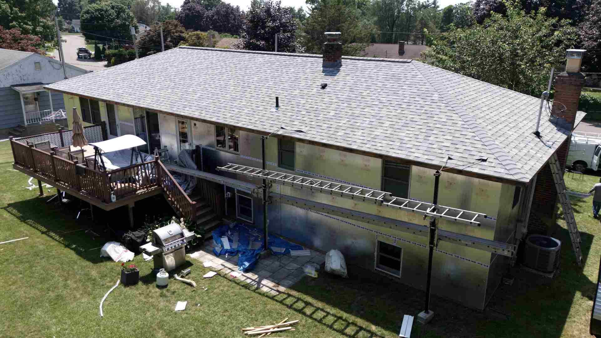 Aerial view of a two-story house with a gray roof, deck, and lawn, with several grills and a ladder outside