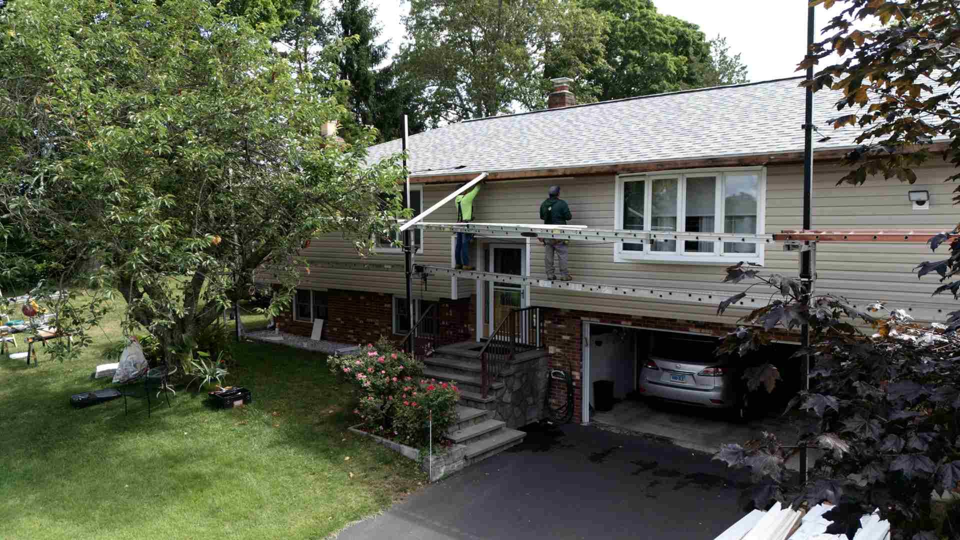 Suburban house with front porch, stairs, and a driveway beneath a leafy tree canopy