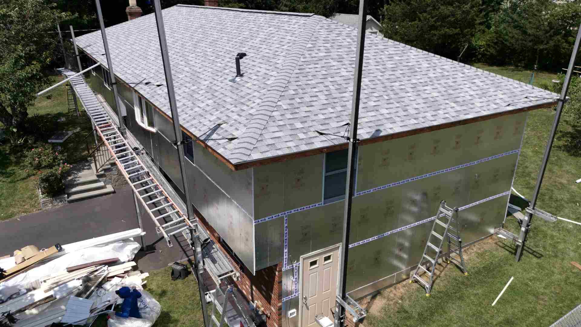 House exterior under construction with roof shingles, scaffolding, and ladders