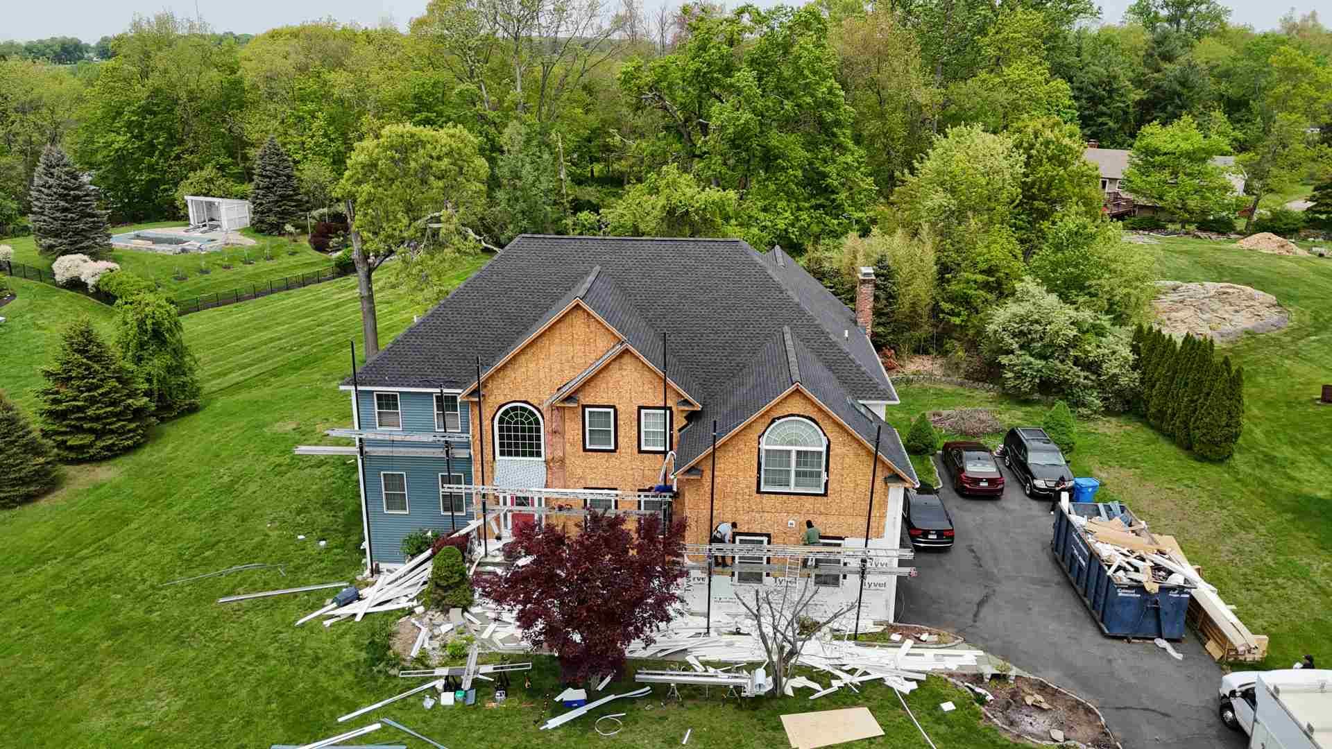 Aerial view of a two-story house with a gray roof, orange siding, and construction materials in the driveway.