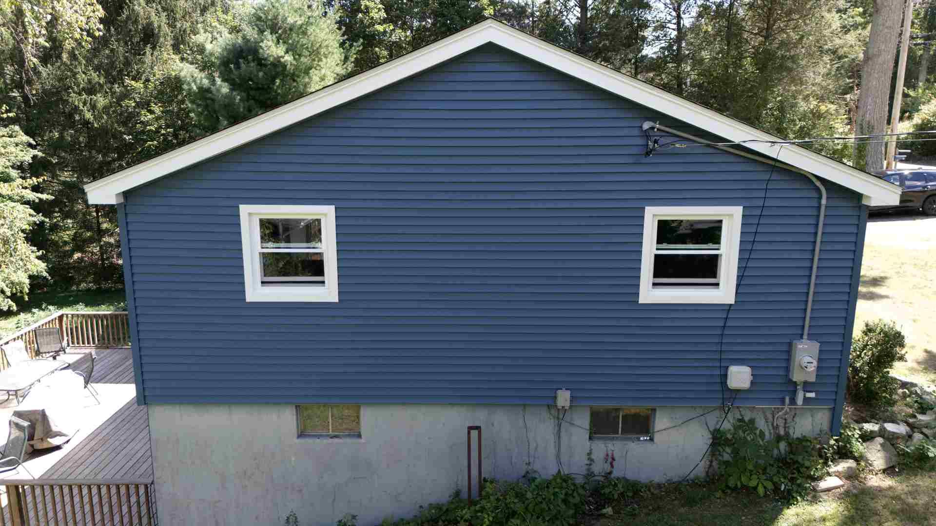 Blue house exterior with two white-trimmed windows and a concrete foundation