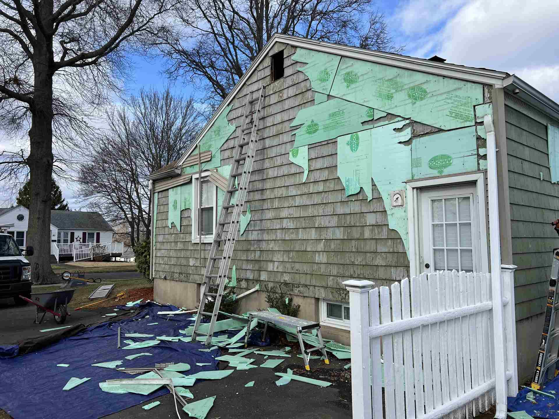 Damaged house with peeling mint-green paint and debris scattered across the porch and walkway.