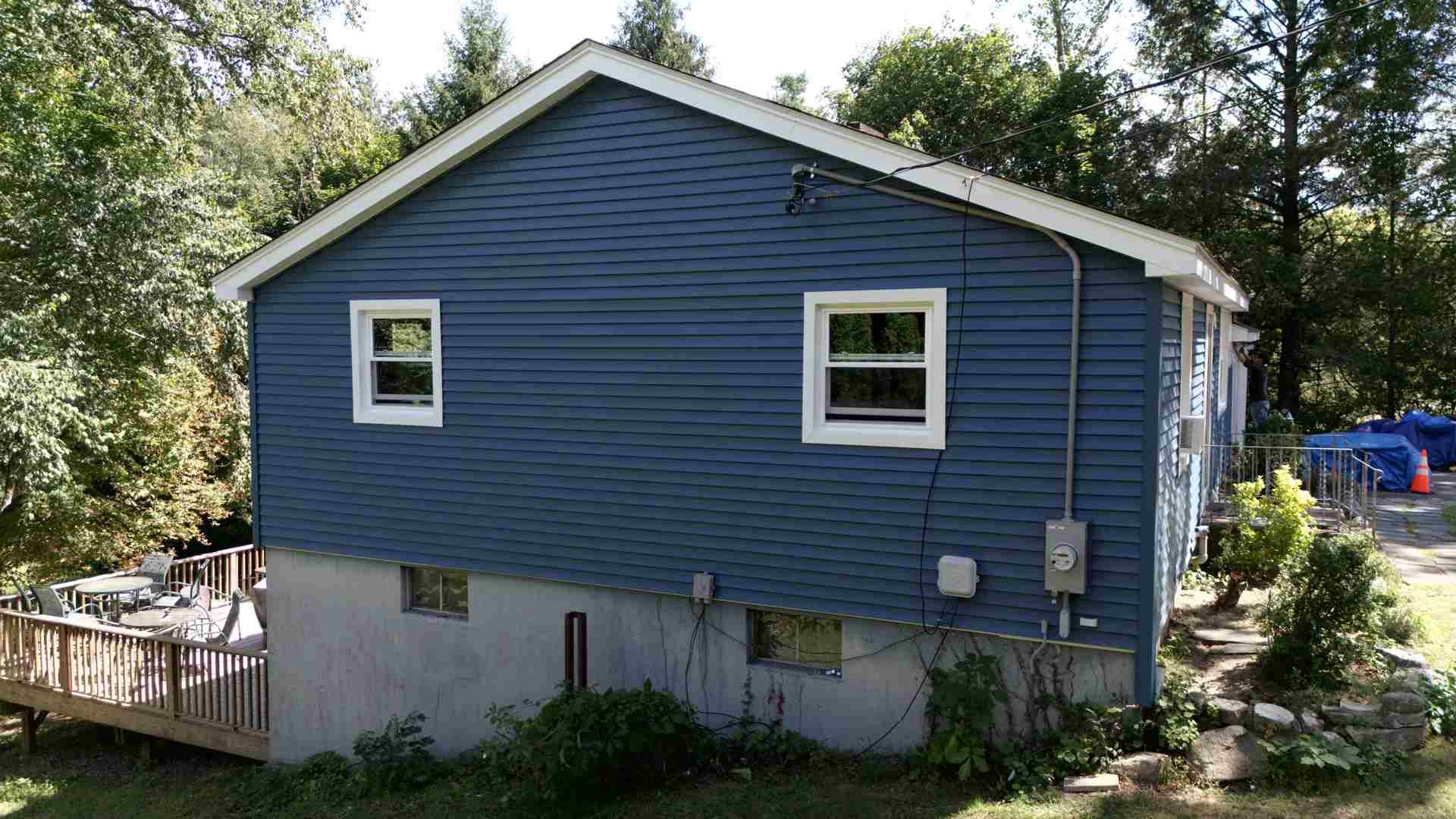Blue house with white trim and small windows, viewed from the side in a wooded yard.