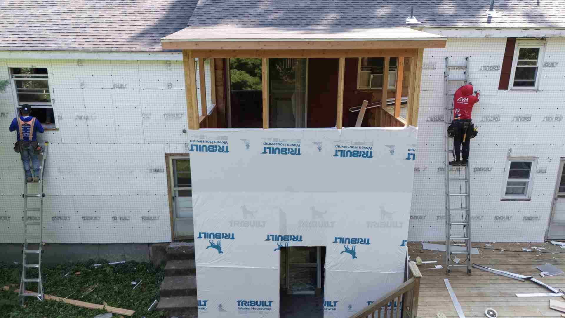 Construction workers on scaffolding installing siding on a house addition under construction