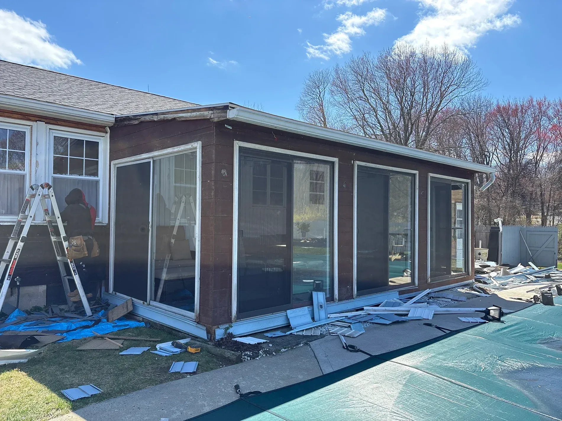 Screened patio enclosure under construction beside a house, with ladders and debris on the ground