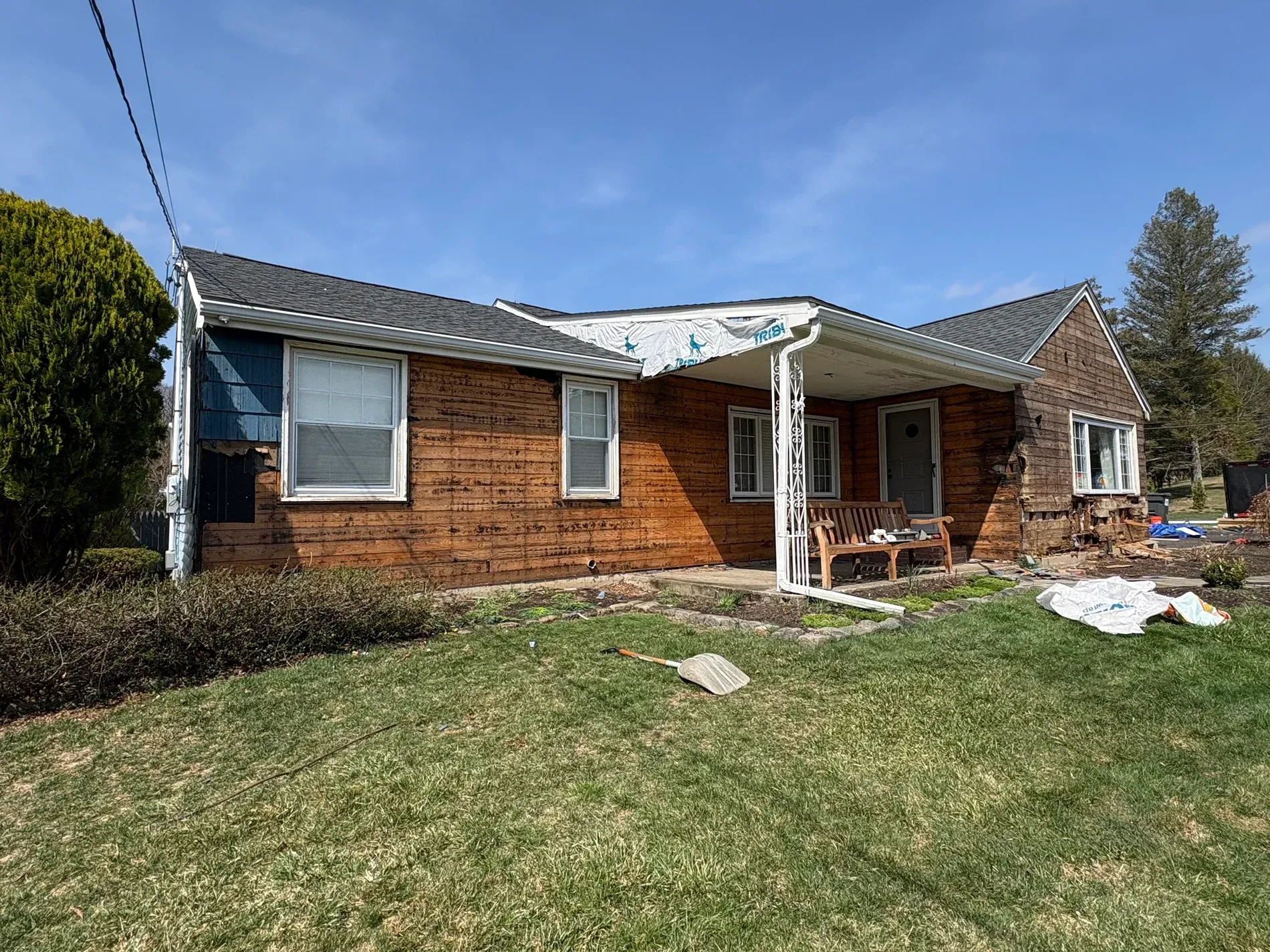 Brick ranch house with white porch, sloped roof, and a grassy front yard under a clear blue sky