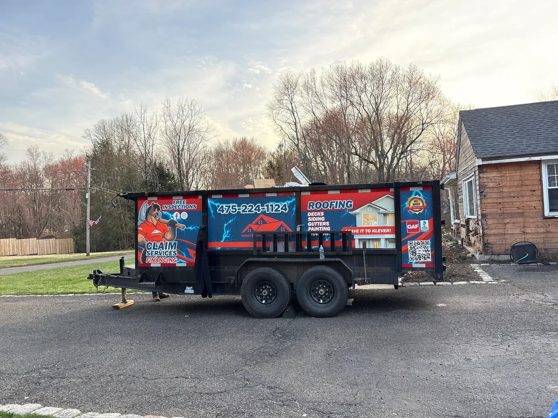 Black trailer with red and blue signage parked on a gravel lot beside a brick building