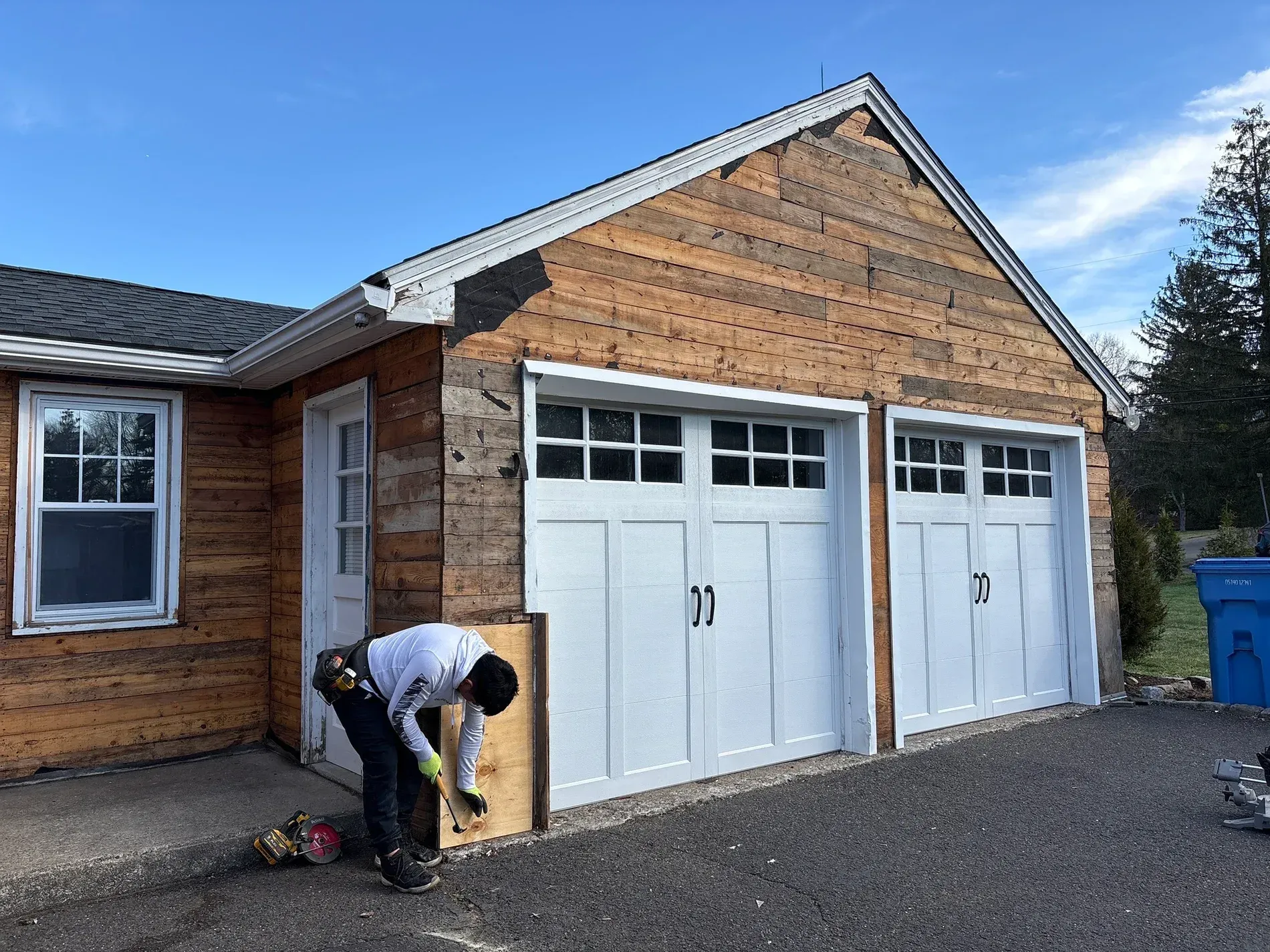 Person painting the trim of a brick garage with white garage doors and a gravel driveway.