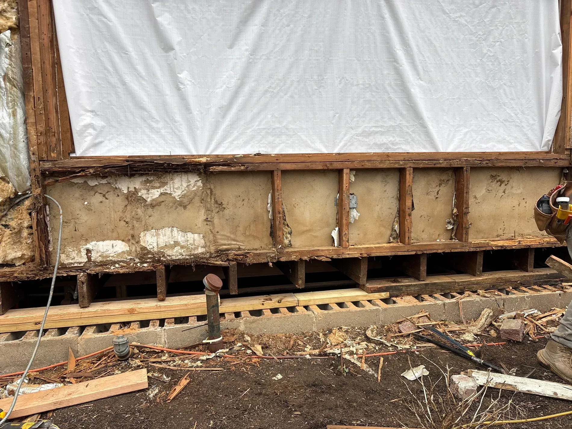 Partially demolished wall with exposed wooden framing, insulation, and construction debris on the ground