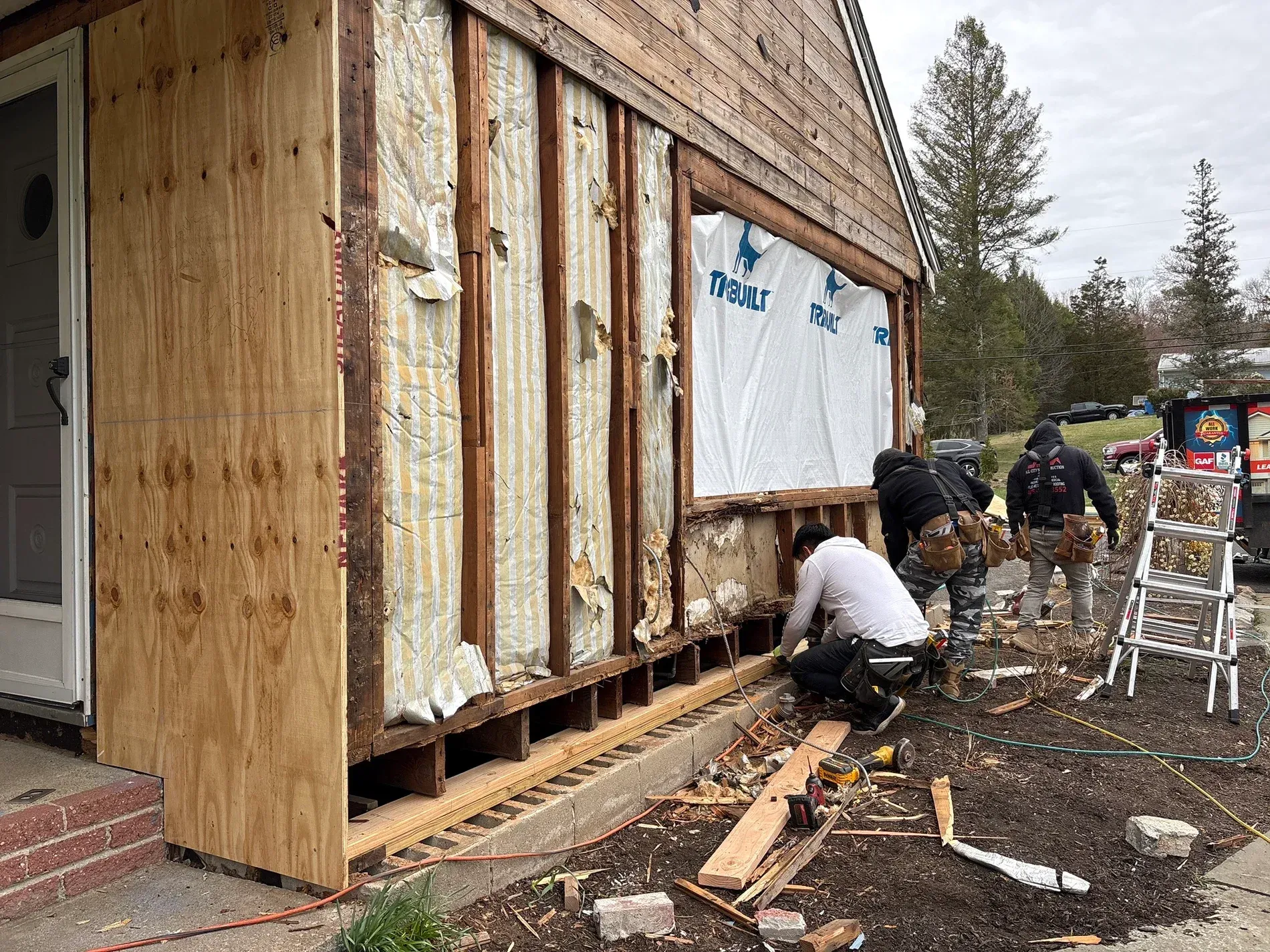 Workers installing wood siding on a small building under construction outdoors