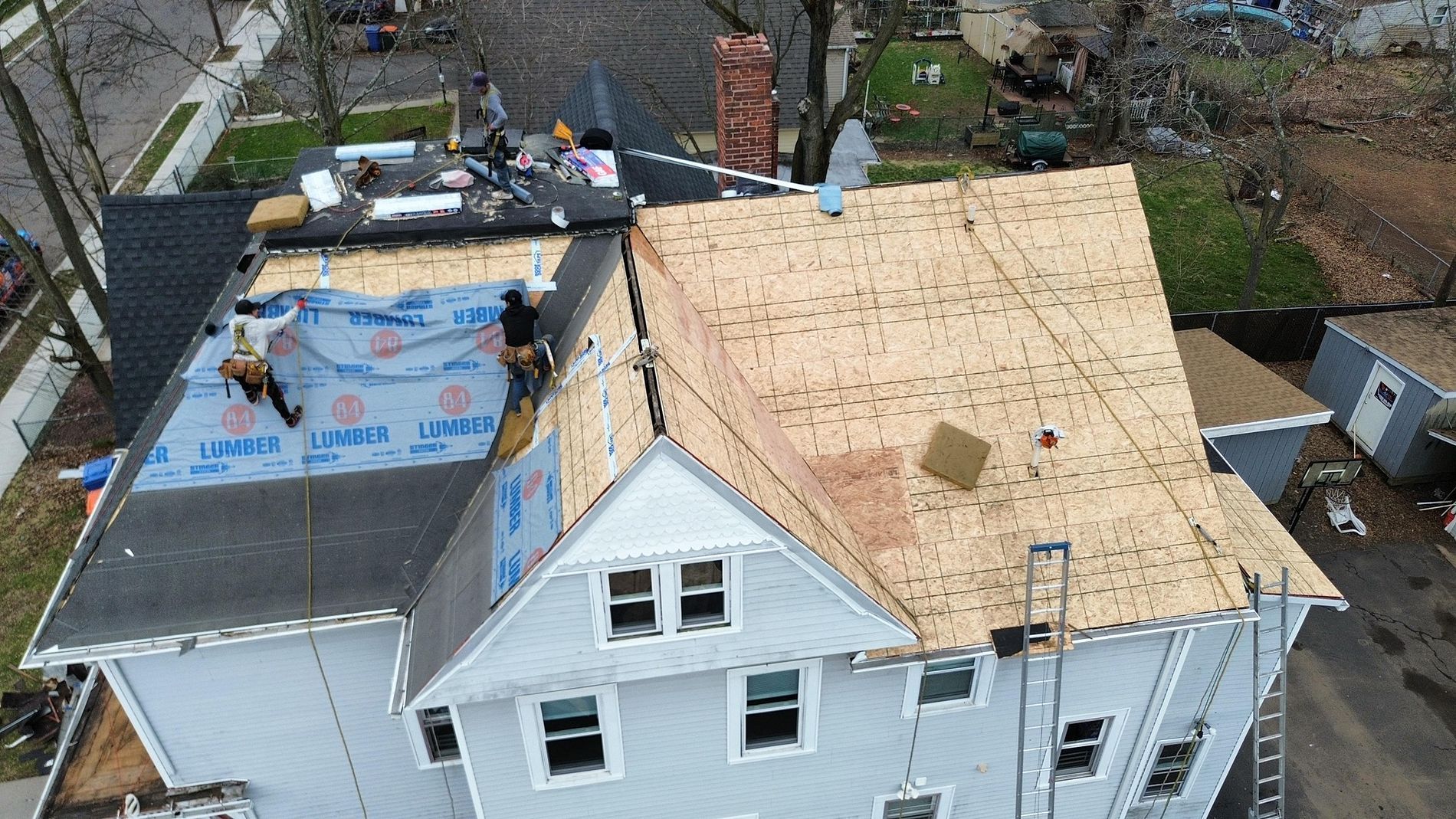 Aerial view of a house roof under repair, with new plywood sheathing and workers on the roof.