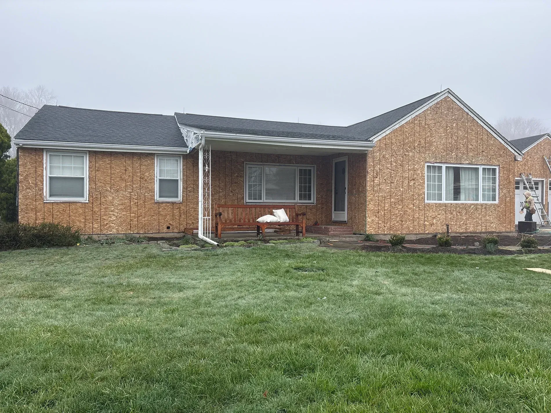 Single-story brick house with a front porch and large green lawn under a cloudy sky
