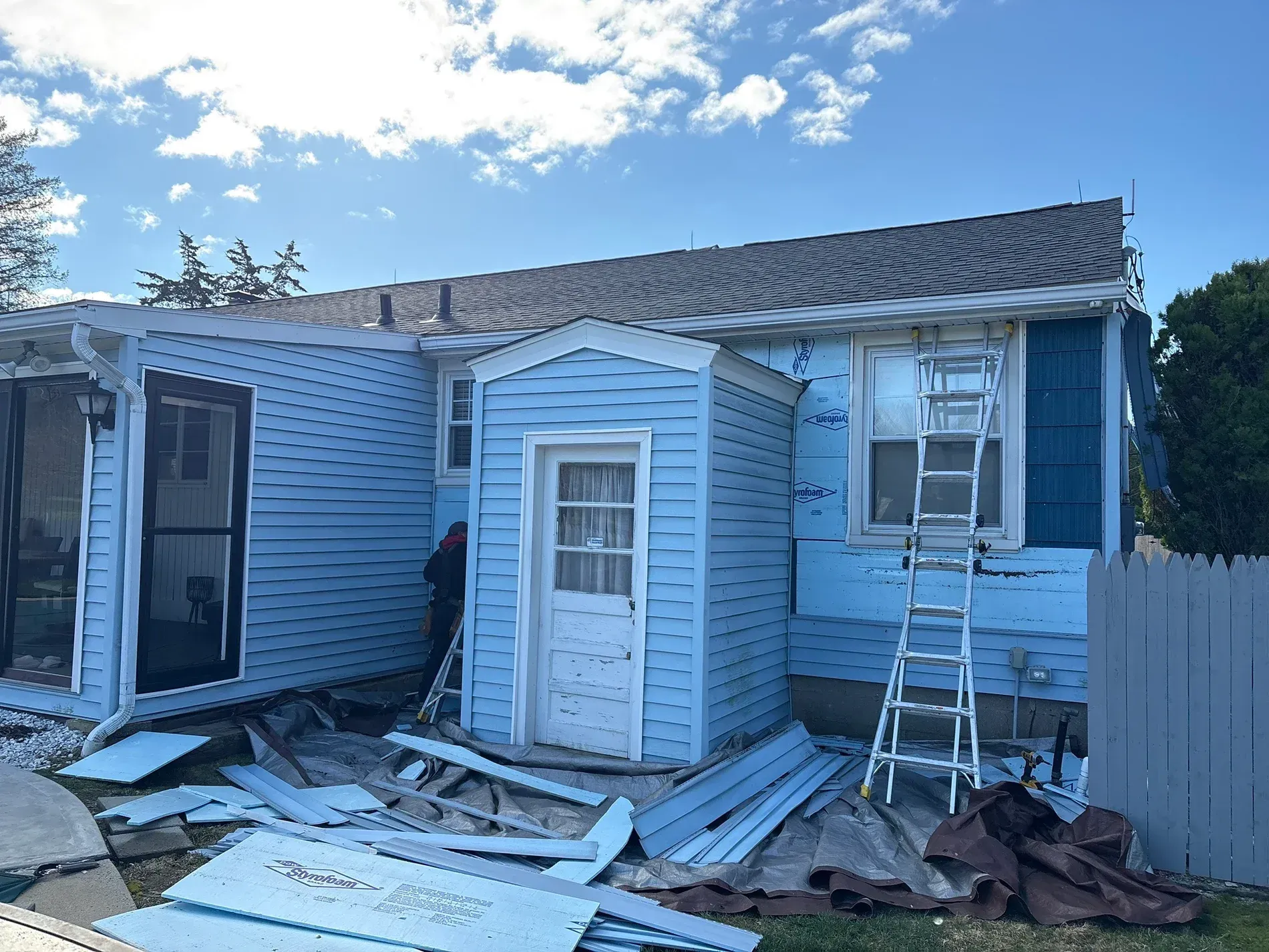 Damaged blue house exterior with debris and broken siding after storm or fire cleanup