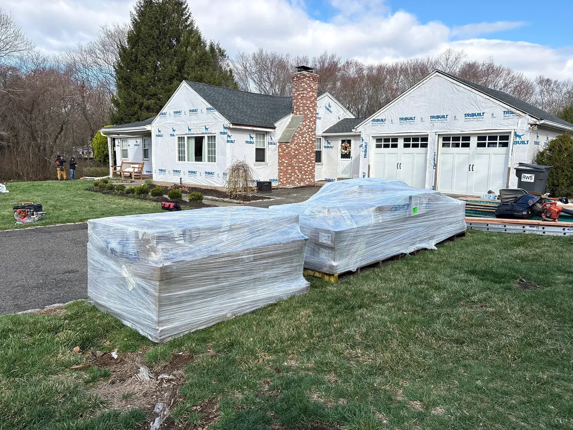 Wrapped furniture sits on a lawn in front of a white house and garage under construction.