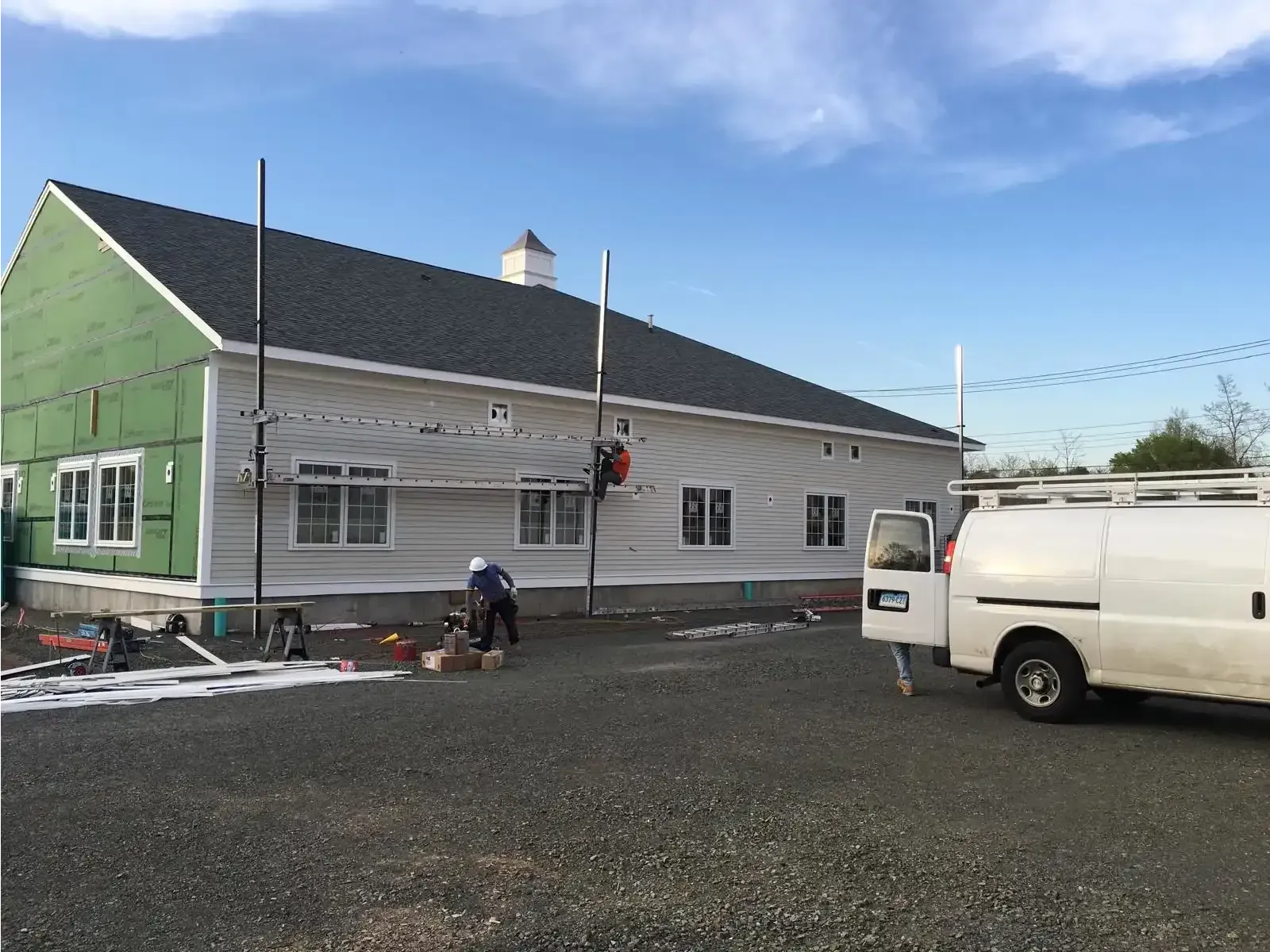 Snow-dusted building with green and white siding, a white van, and a person near the entrance under a blue sky