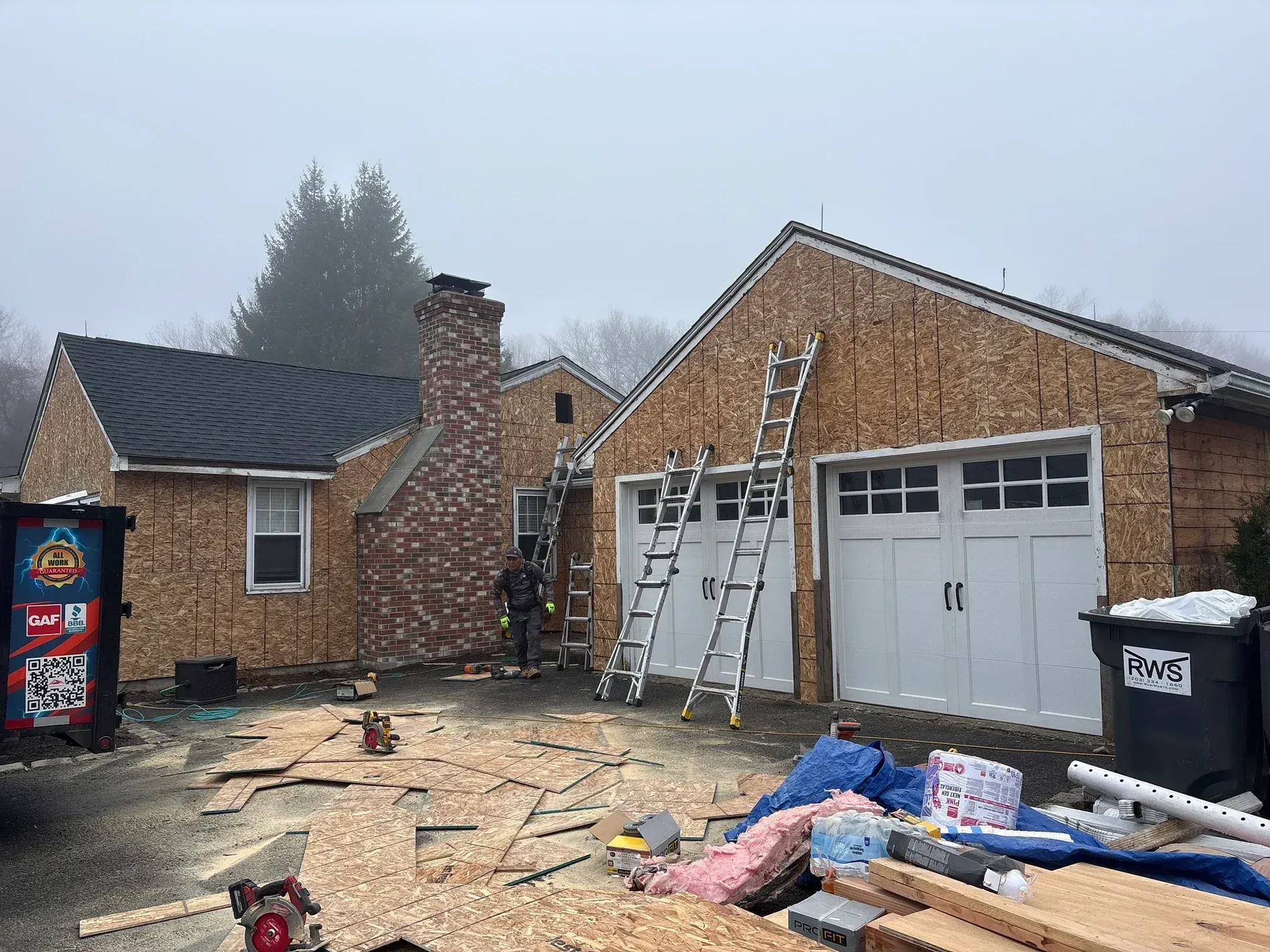 Brick house under construction with ladders, scattered materials, and a damaged garage door